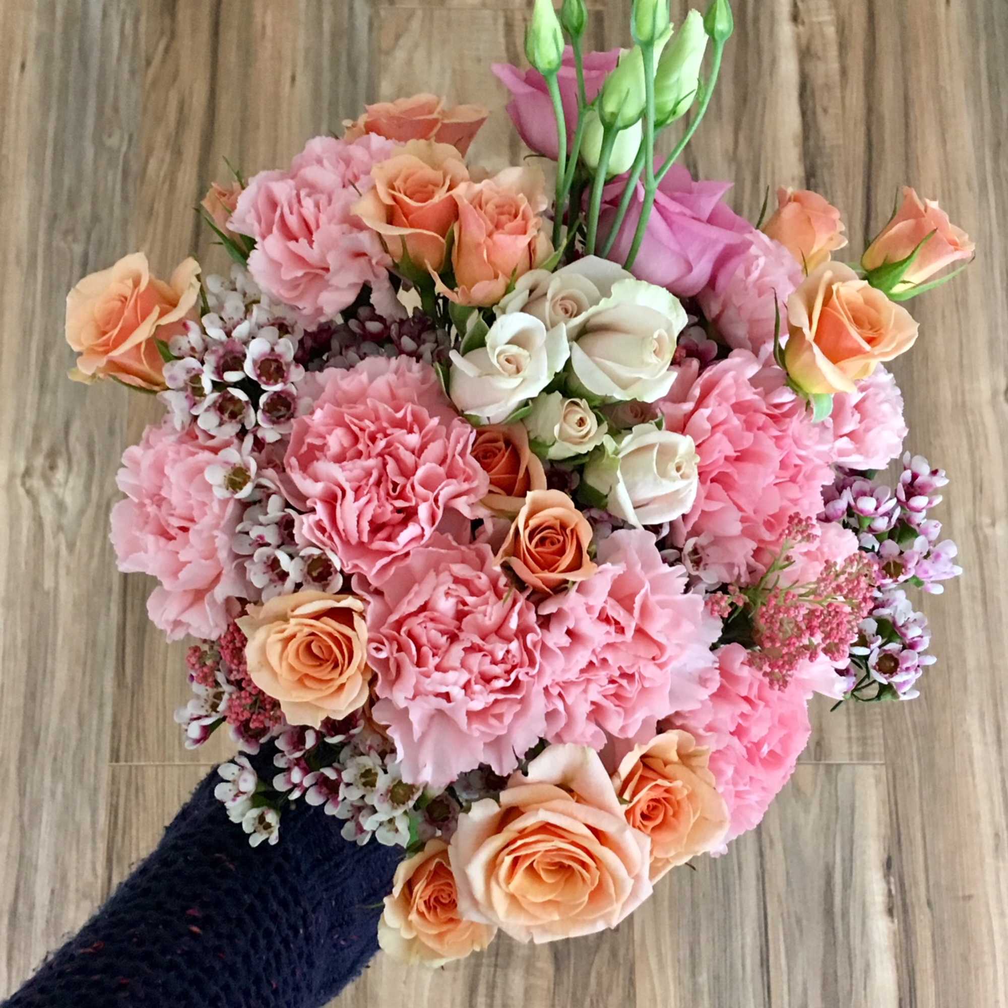 Handheld bouquet of pink carnations and peach roses with white blooms
