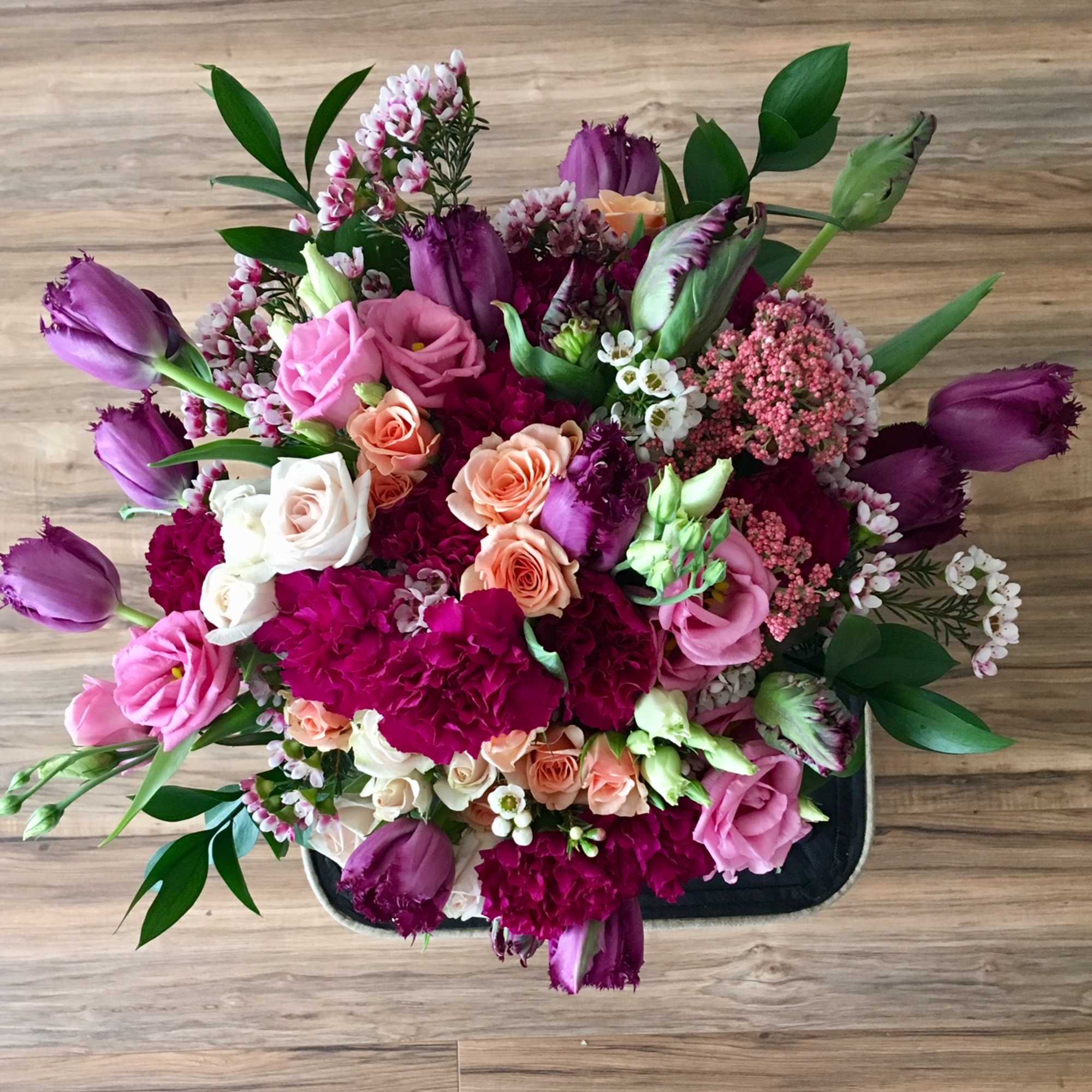 Mixed bouquet of pink, purple, and peach flowers in a black tray