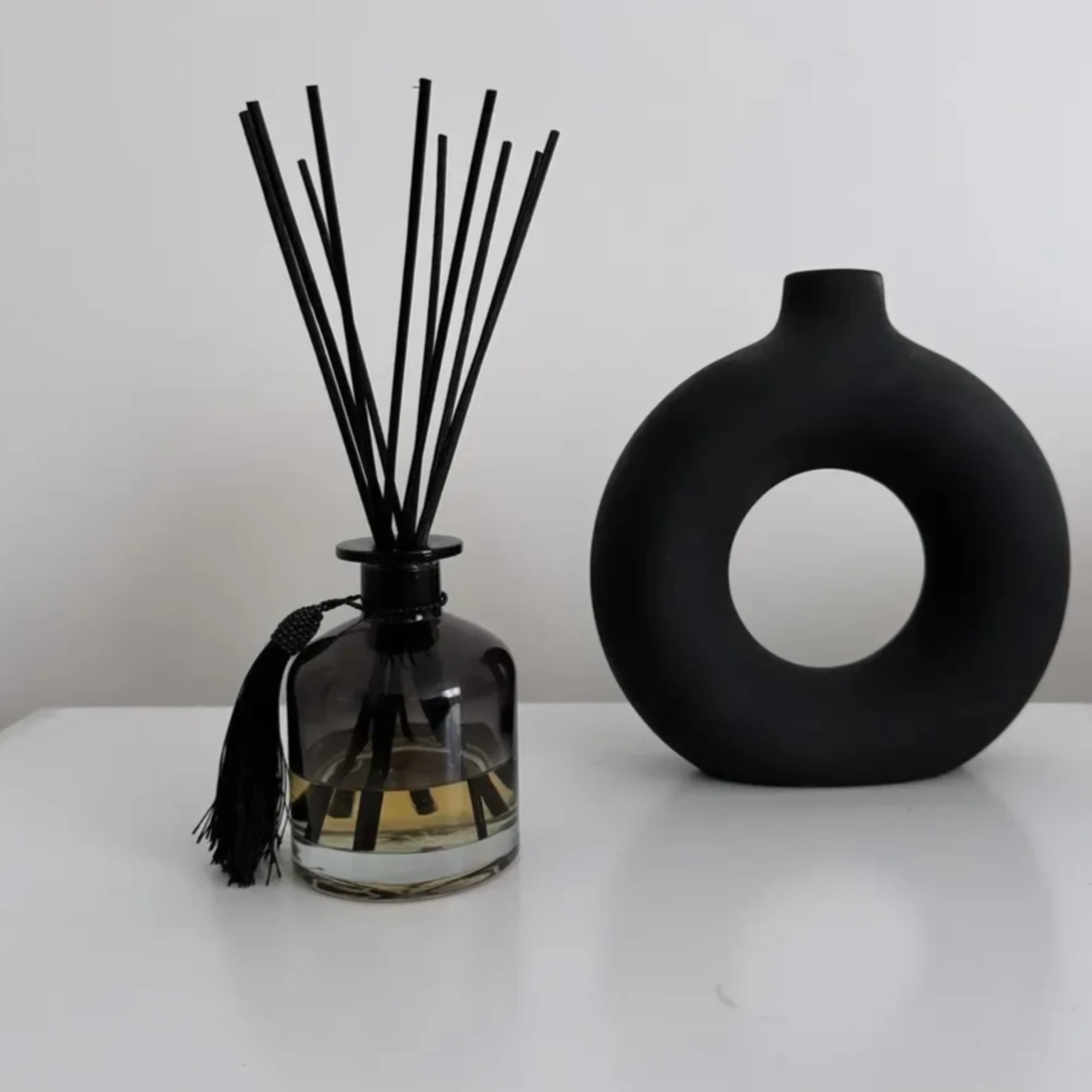 Black reed diffuser bottle with a round black vase beside it