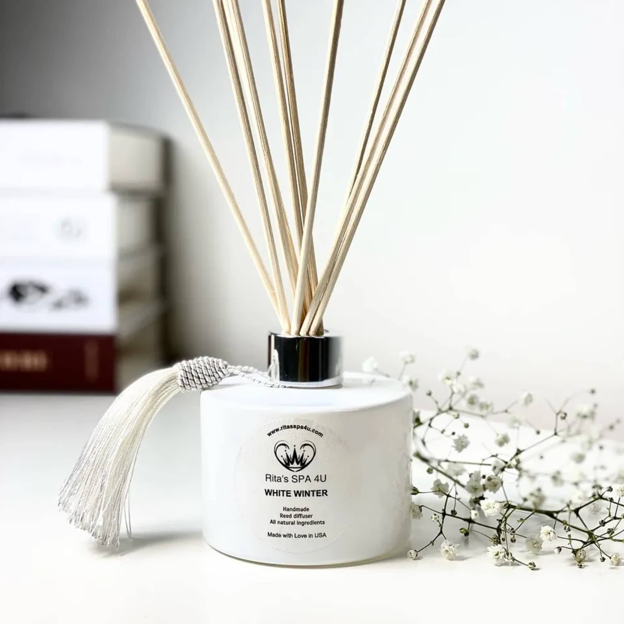 White reed diffuser with a tassel and small white flowers beside it
