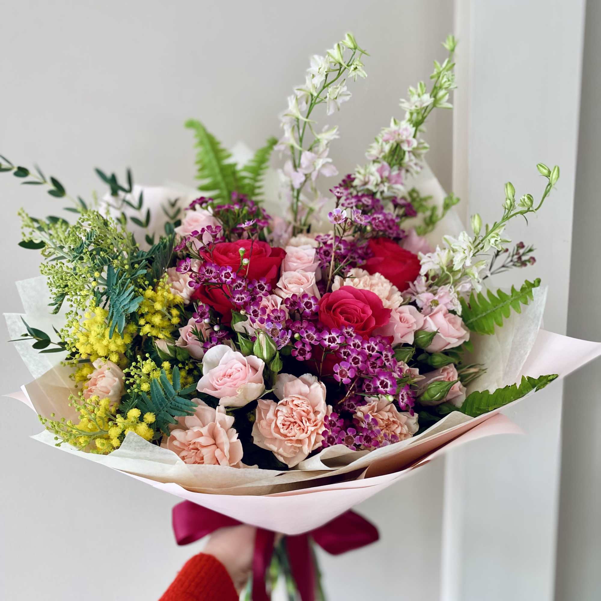 Hand-tied bouquet of pink and red roses with purple accents