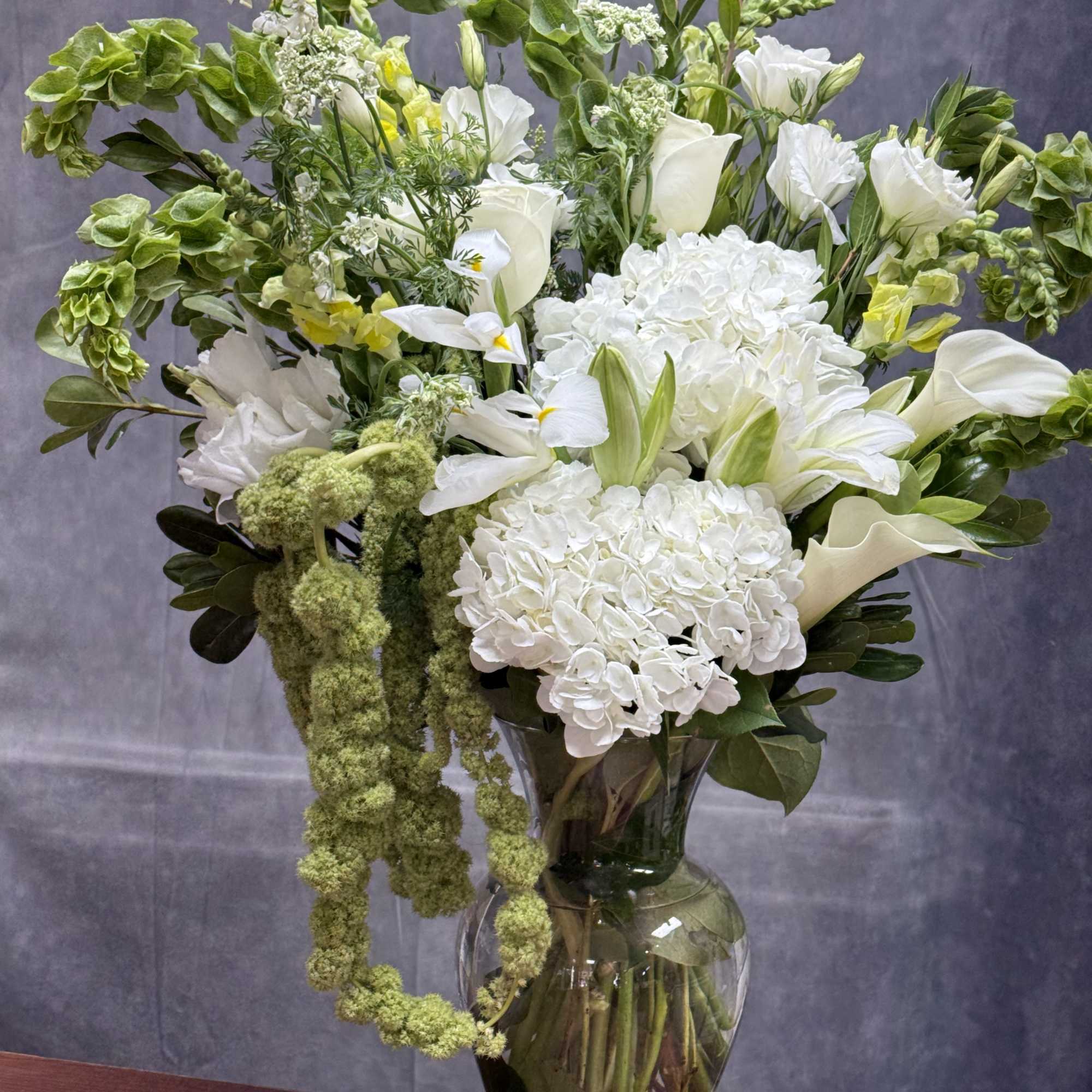 White flowers and green accents arranged in a clear glass vase