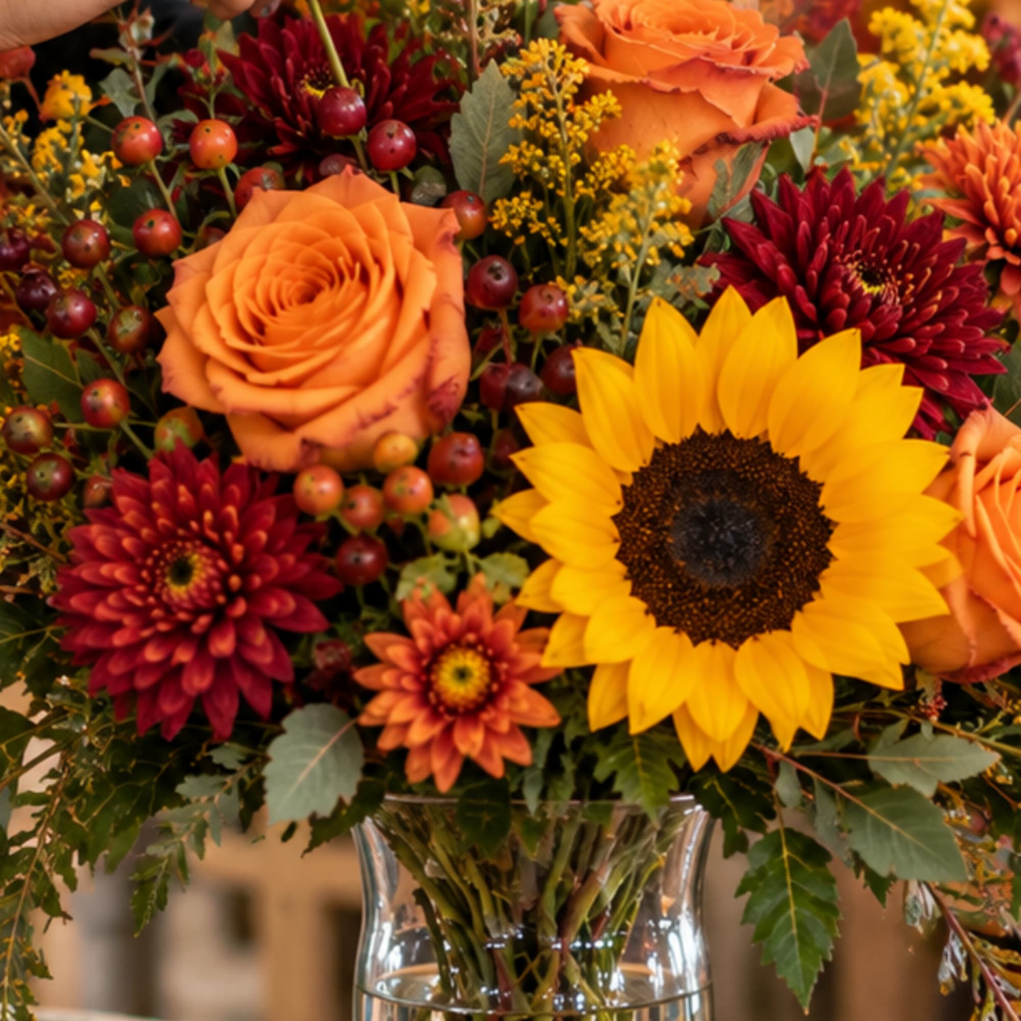 Autumn bouquet with sunflowers, orange roses, and burgundy mums in a glass vase