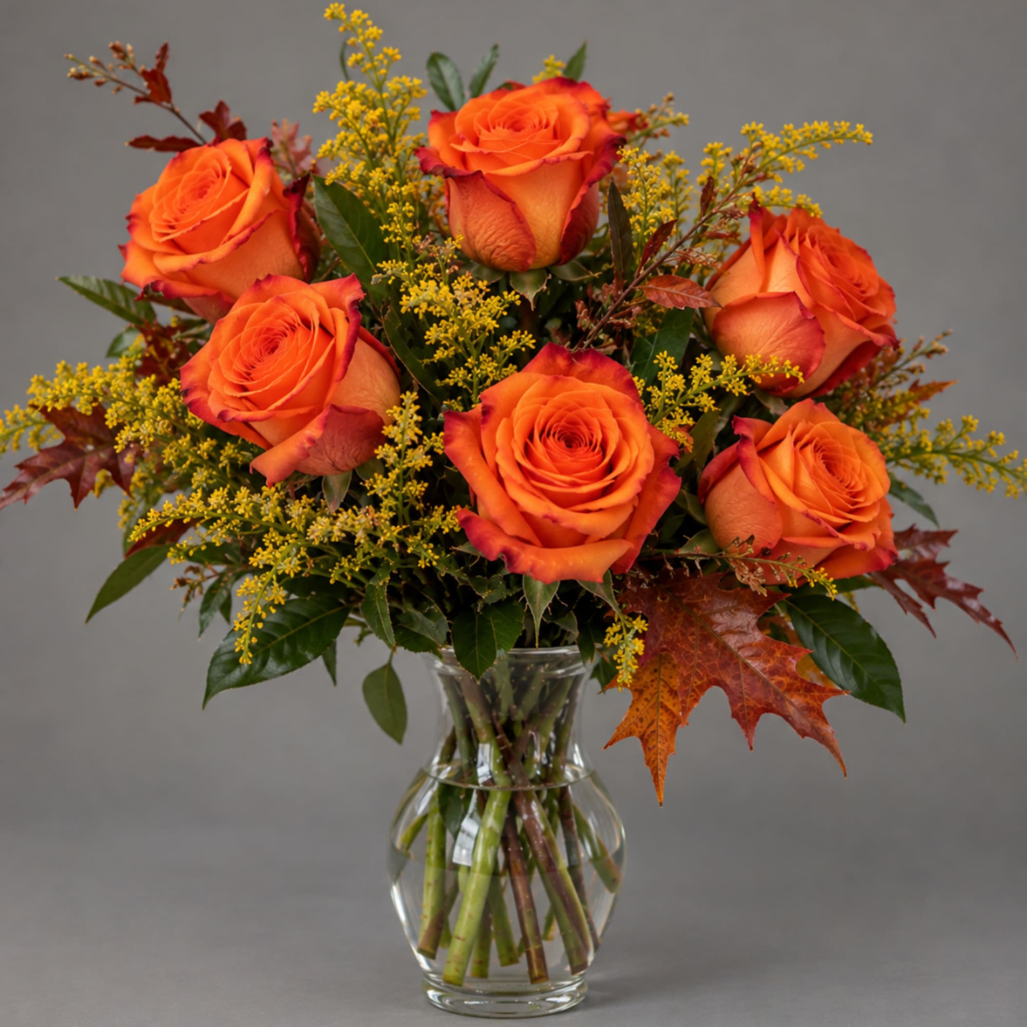 Orange roses in a clear glass vase with yellow filler flowers