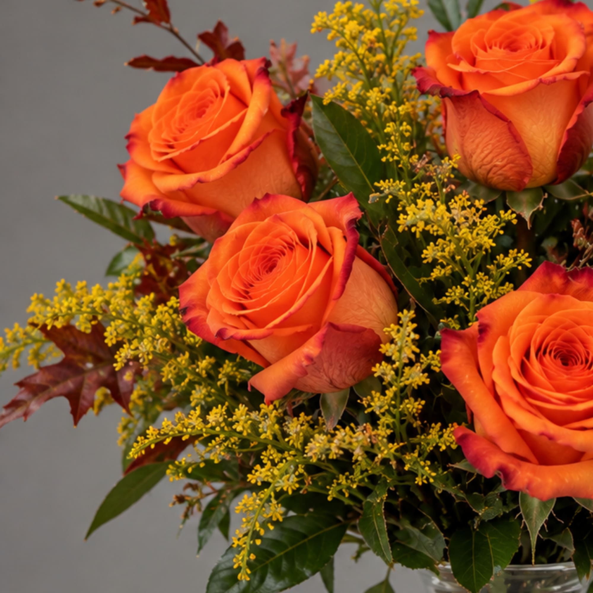 Bouquet of orange roses with yellow filler flowers in a glass vase