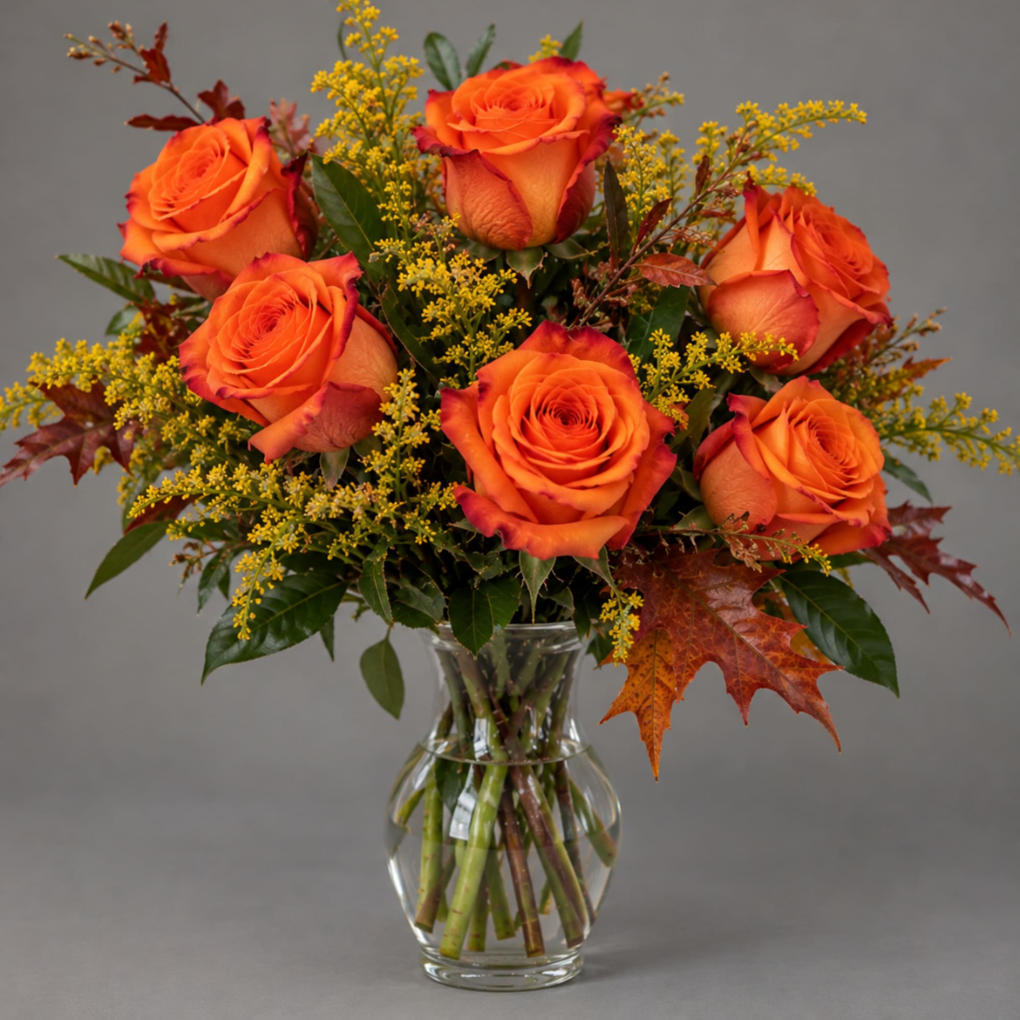 Orange roses in a clear glass vase with yellow filler flowers, photo 4 of 4