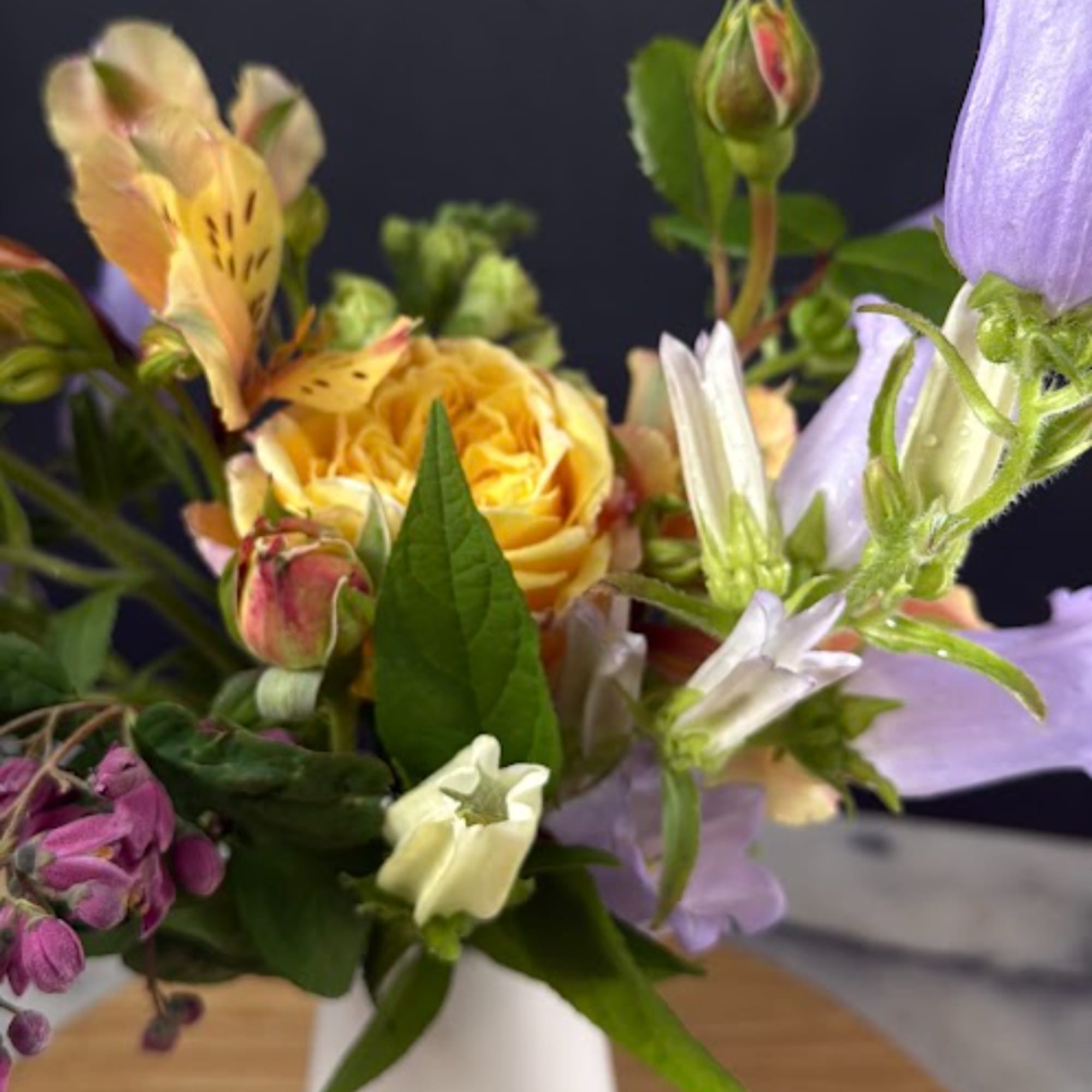 Mixed bouquet with yellow roses and purple bellflowers in a white vase