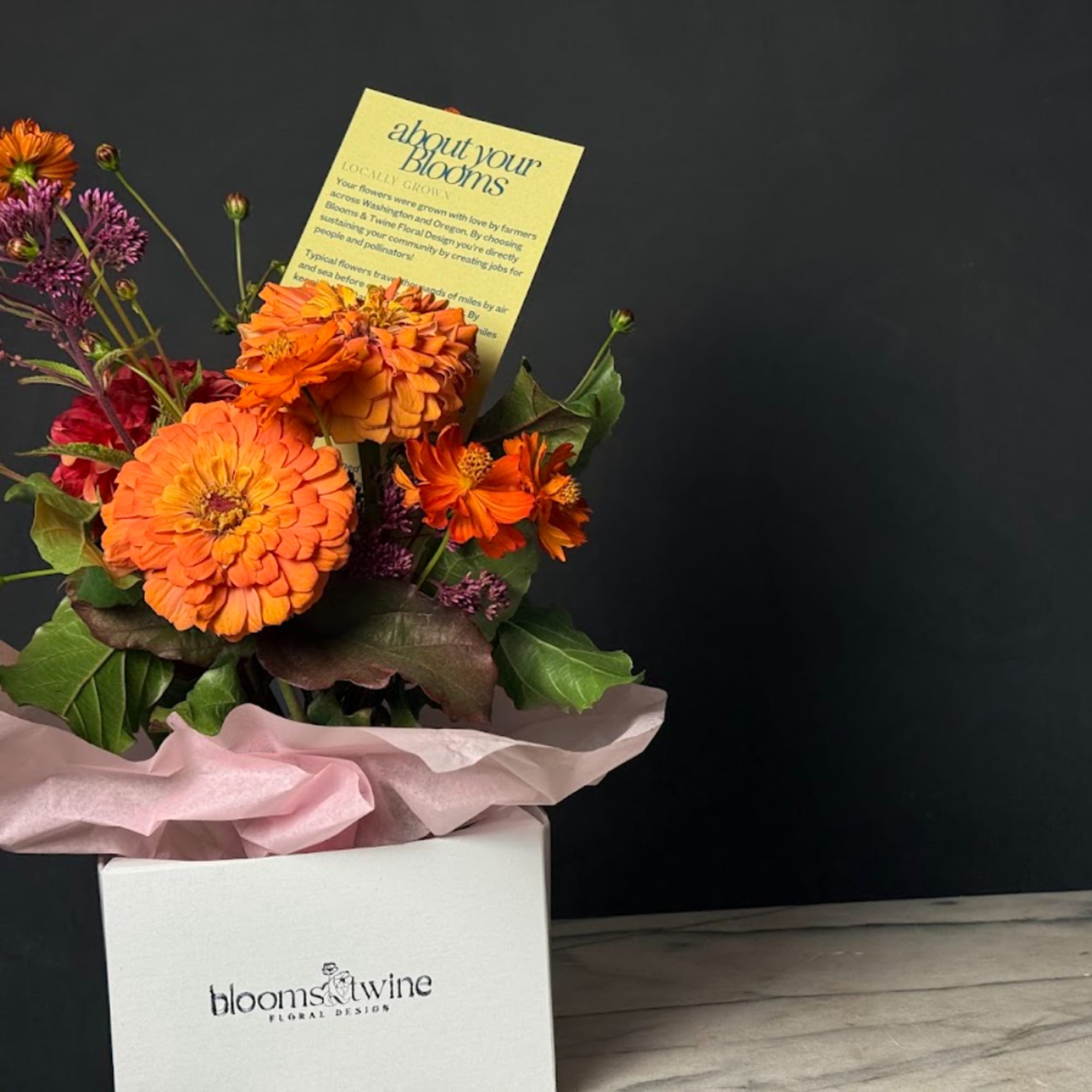 Orange and purple flowers in a white gift box with pink tissue paper