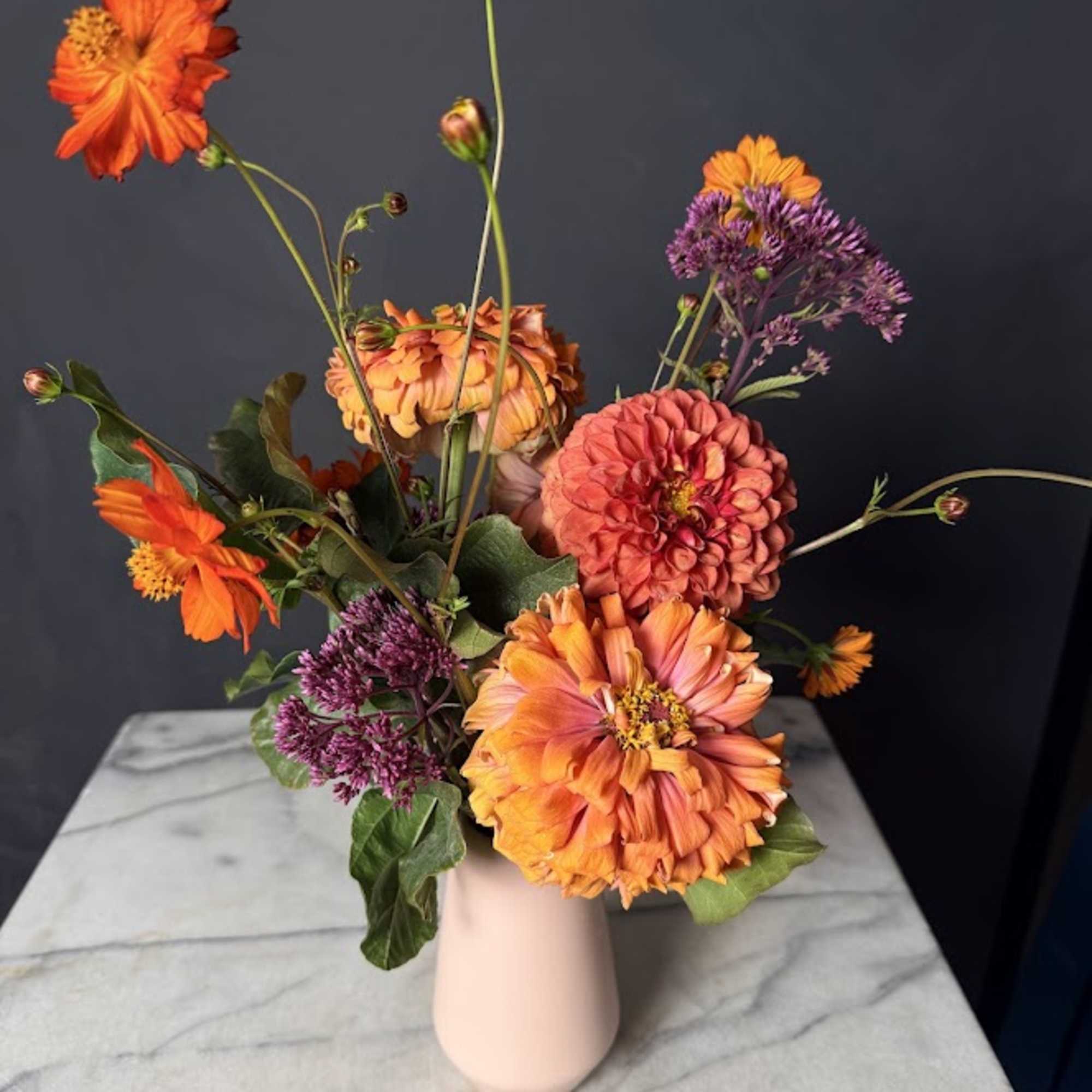 Orange and pink flowers arranged in a pale vase