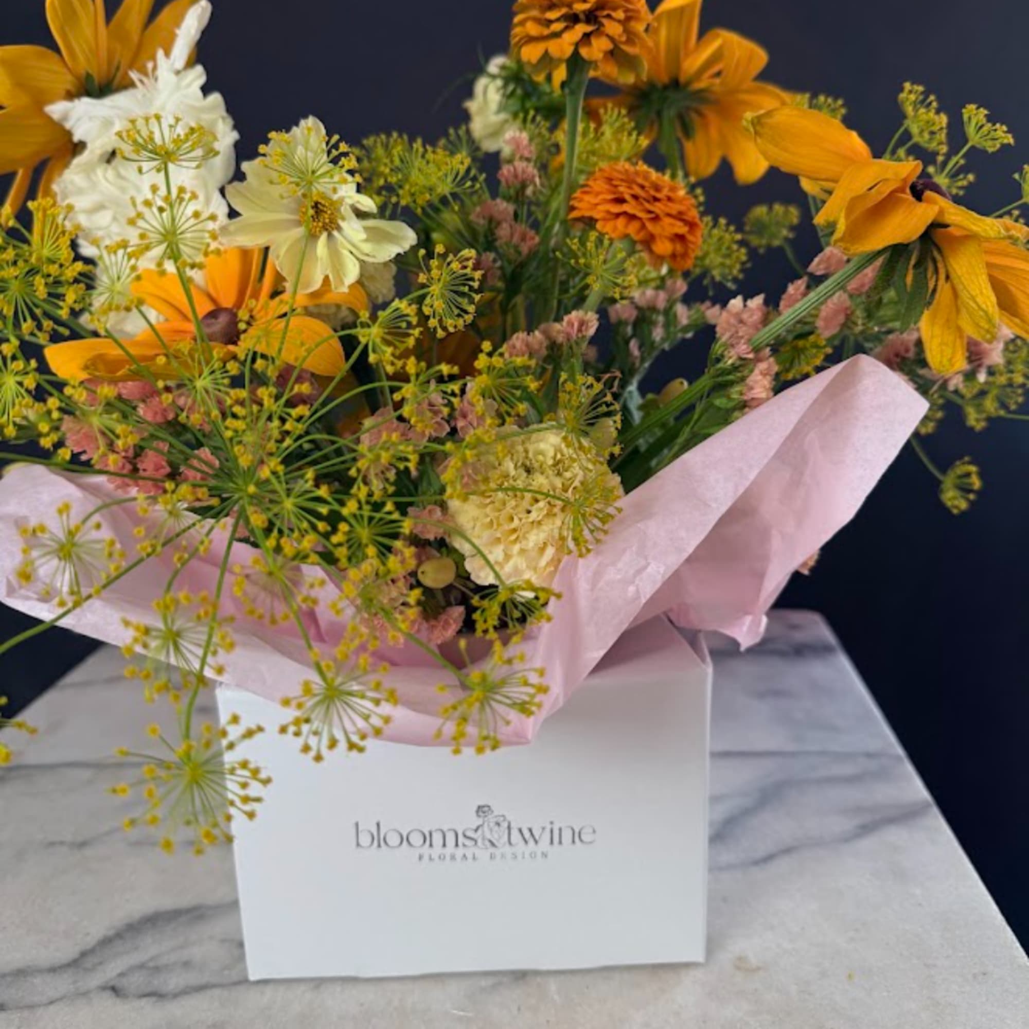 Bouquet of yellow and white flowers in pink wrapping inside a white box