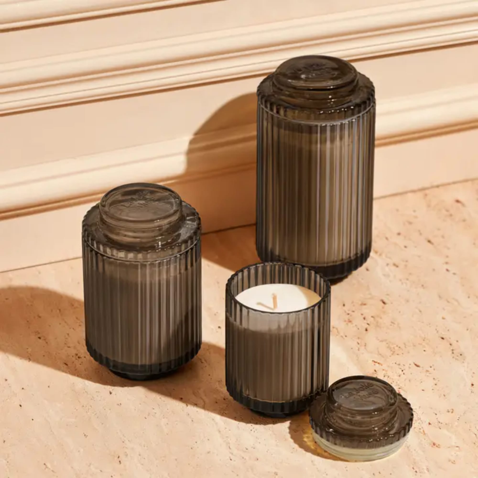 Four ribbed glass candles and lids on a beige surface
