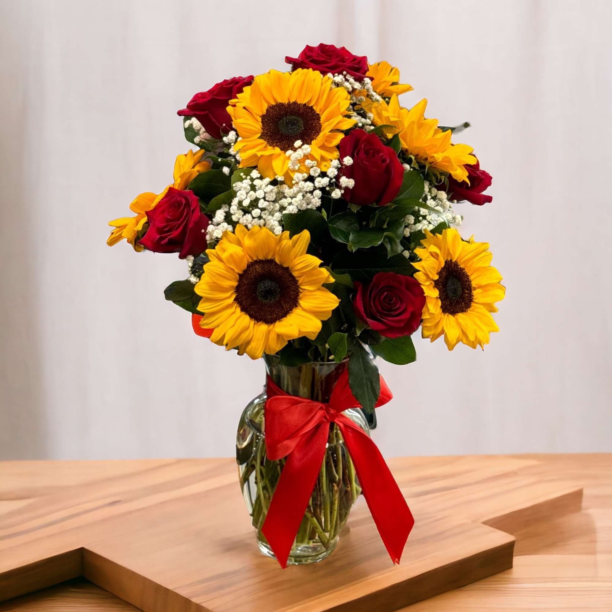 Bouquet of red roses and yellow sunflowers in a glass vase with a red ribbon