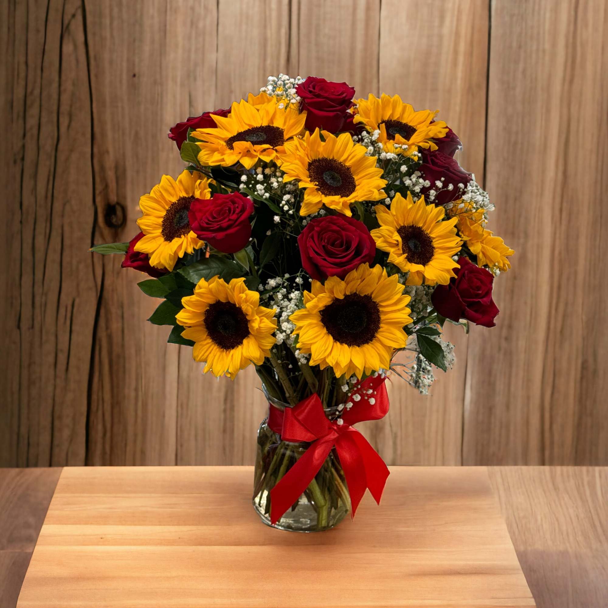 Bouquet of sunflowers and red roses in a glass vase with a red ribbon