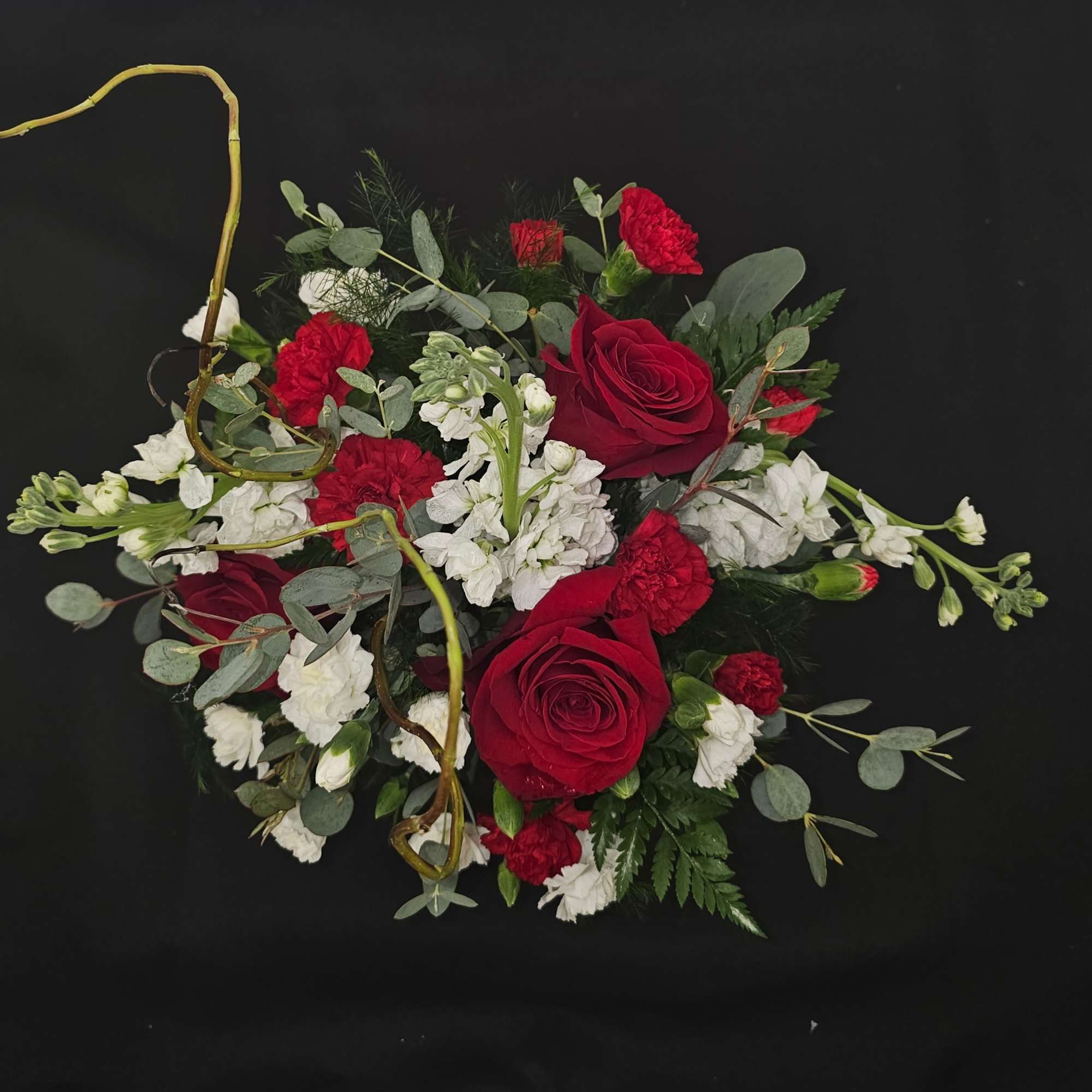 Red roses and white carnations arranged with eucalyptus on a black background