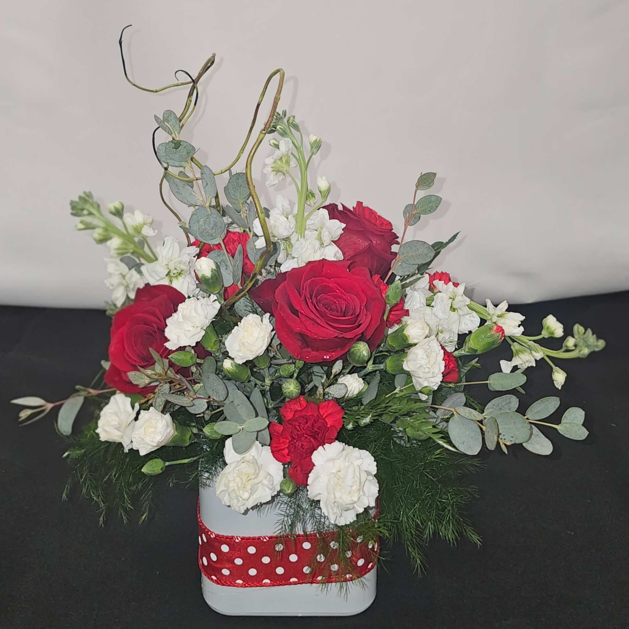 Red roses and white carnations in a white container with a red polka-dot ribbon
