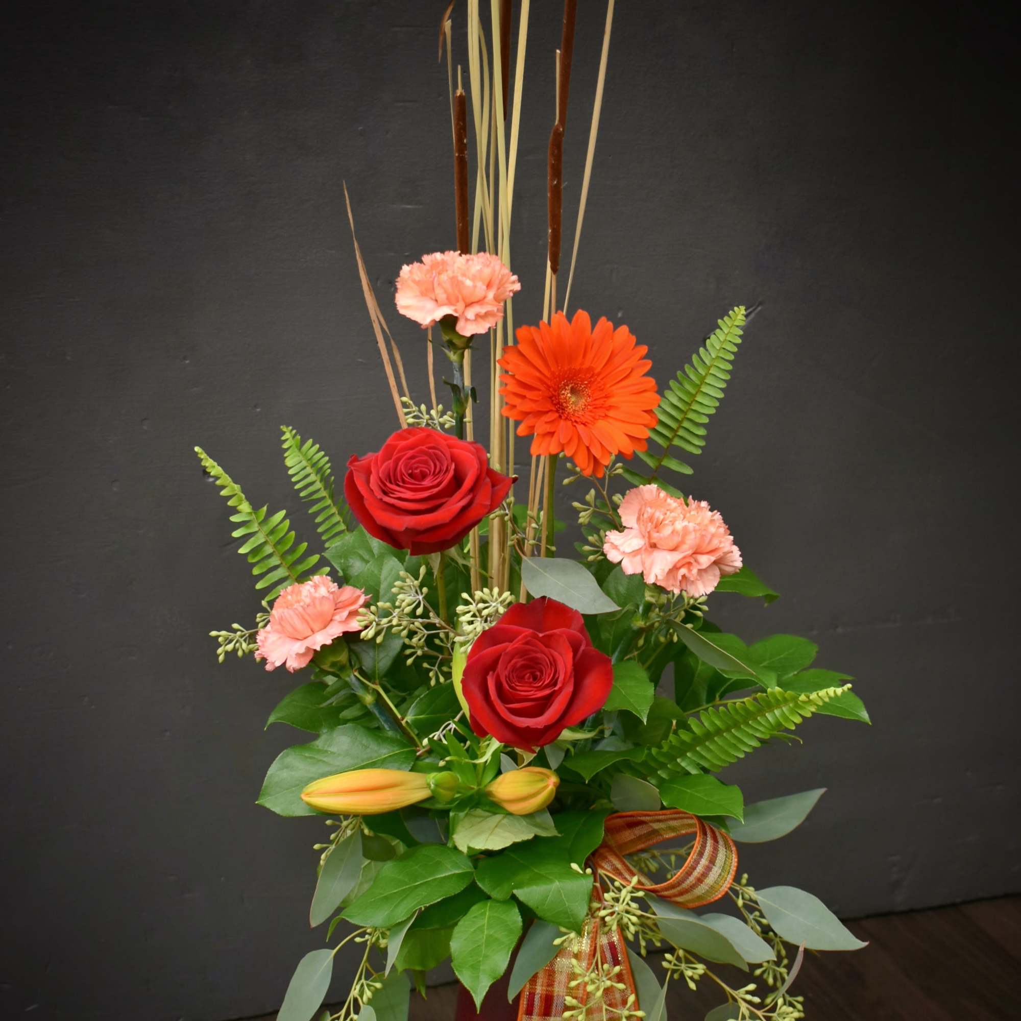 Tall red and peach floral arrangement in a burgundy vase with ribbon