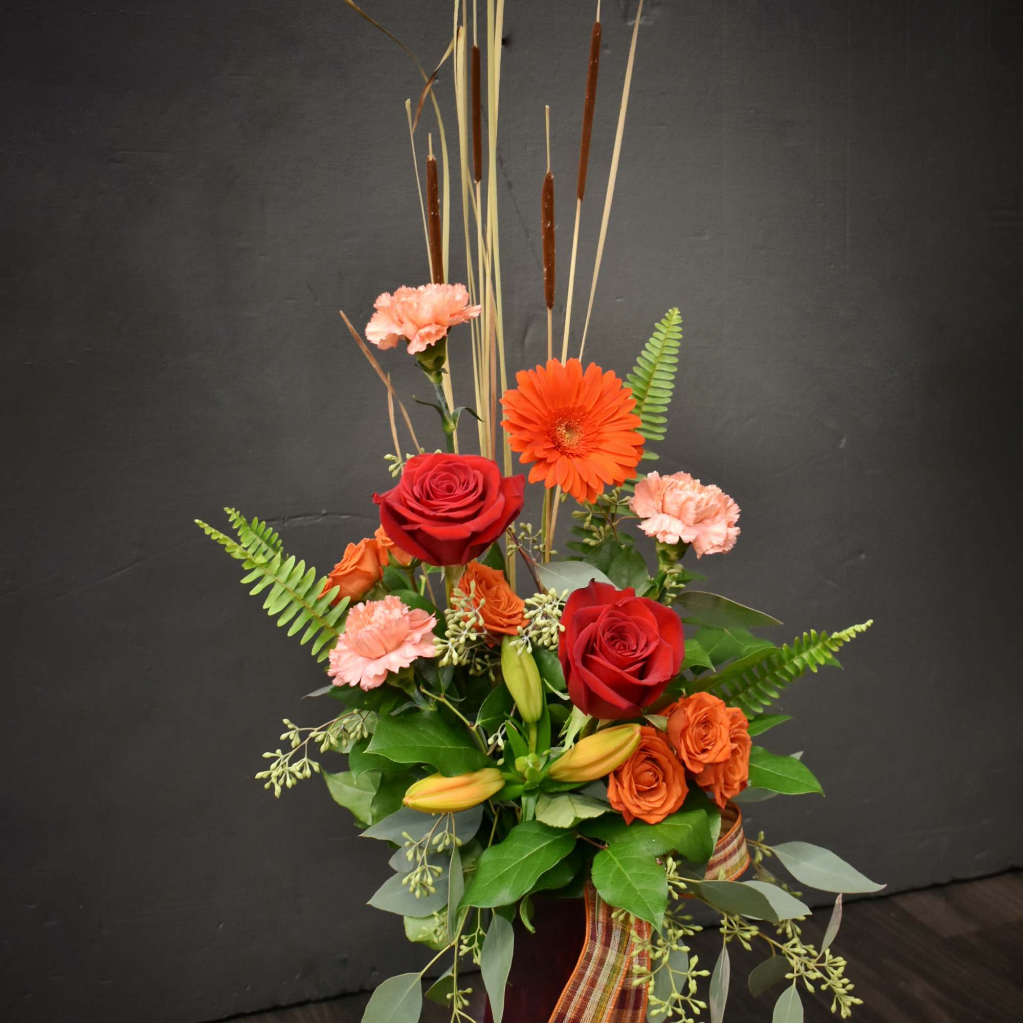 Tall floral arrangement with red roses, orange gerbera daisies, and pink carnations in a red vase
