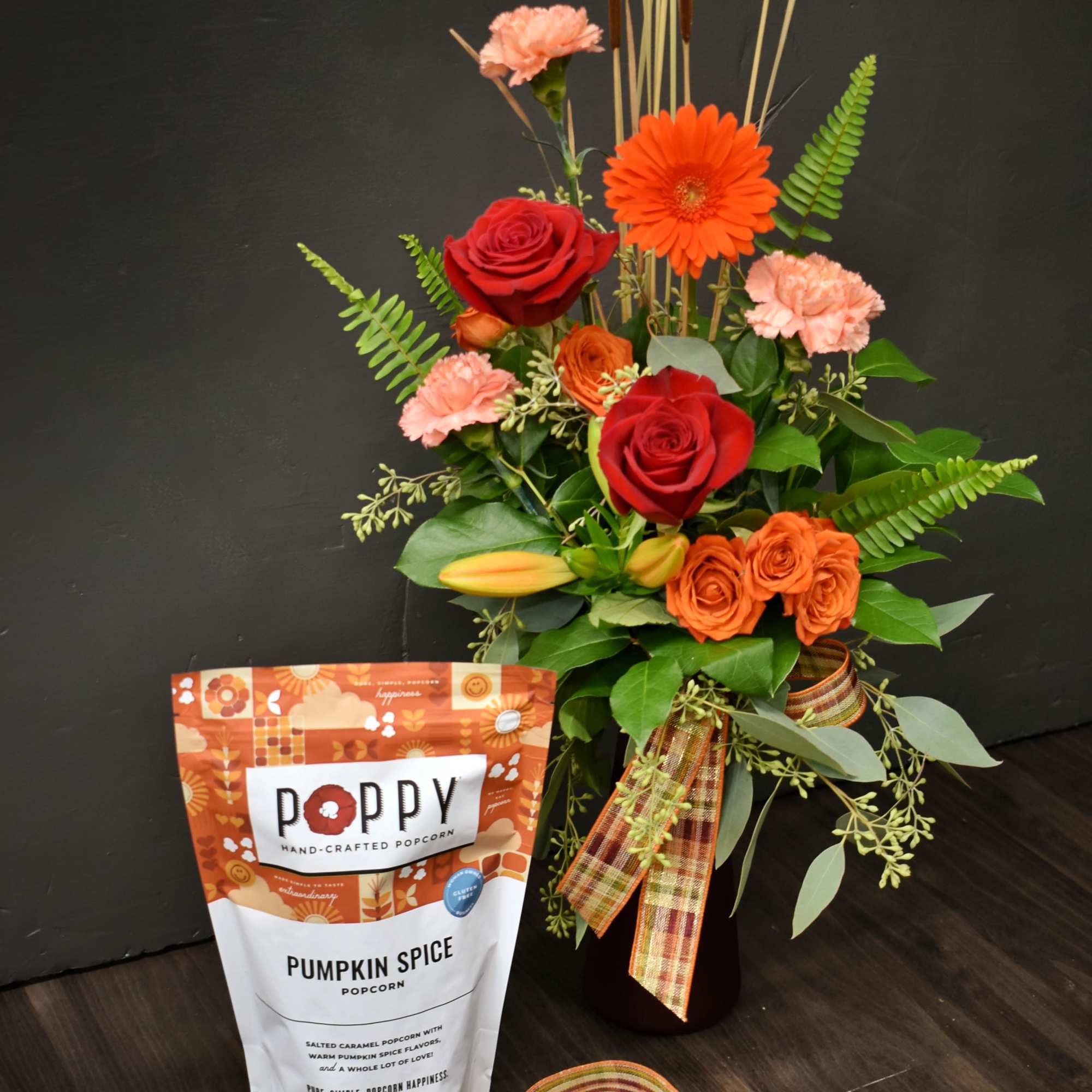 Floral arrangement with red roses, orange gerbera daisies, and popcorn gift bag