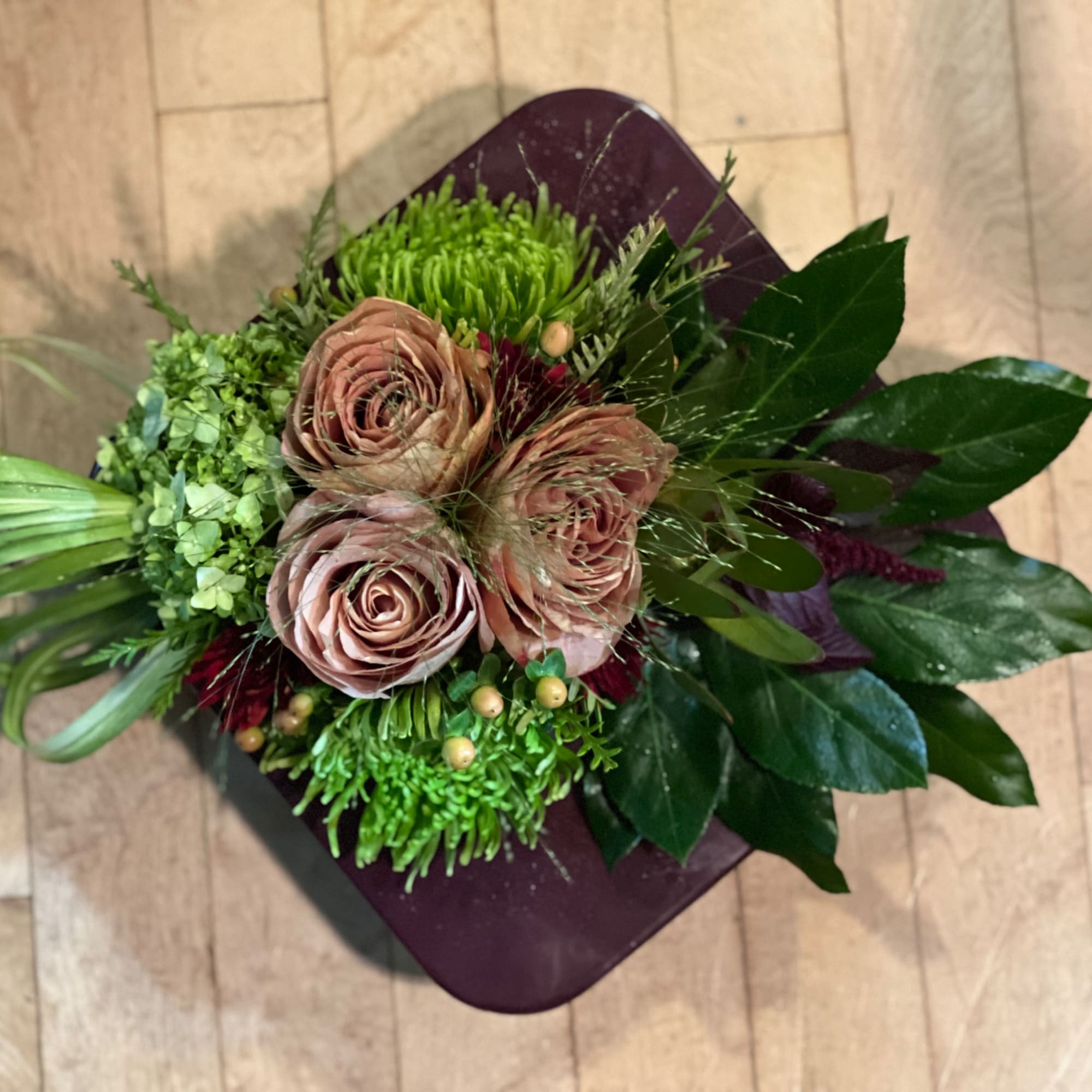 Compact bouquet of blush roses and green blooms on a dark square base