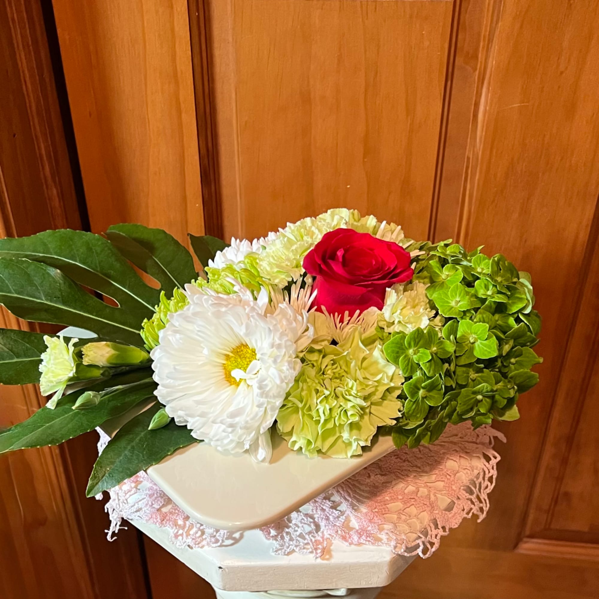Floral arrangement with a red rose, white blooms, and green hydrangea in a white container
