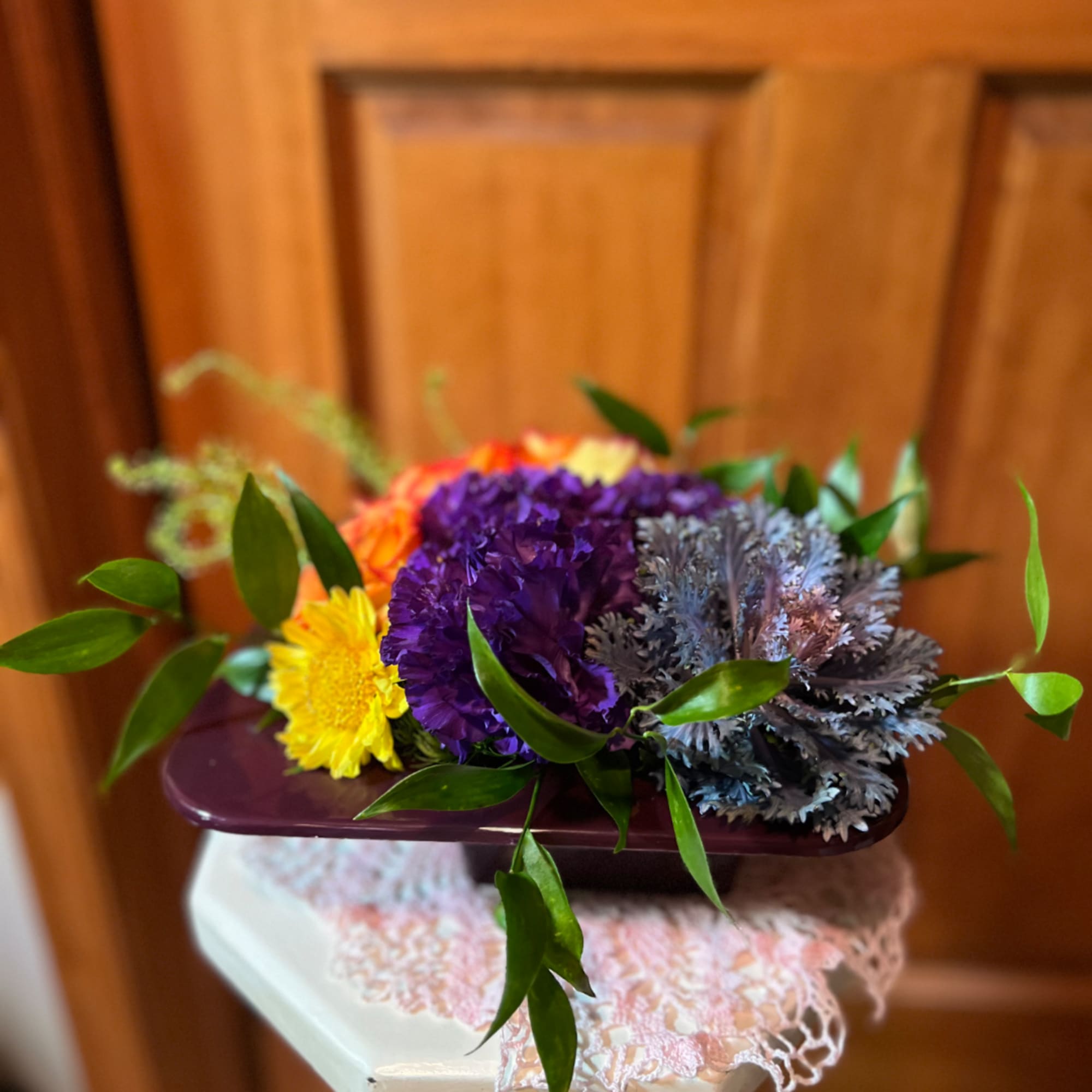 Colorful bouquet in a purple rectangular vase with yellow, purple, and orange blooms