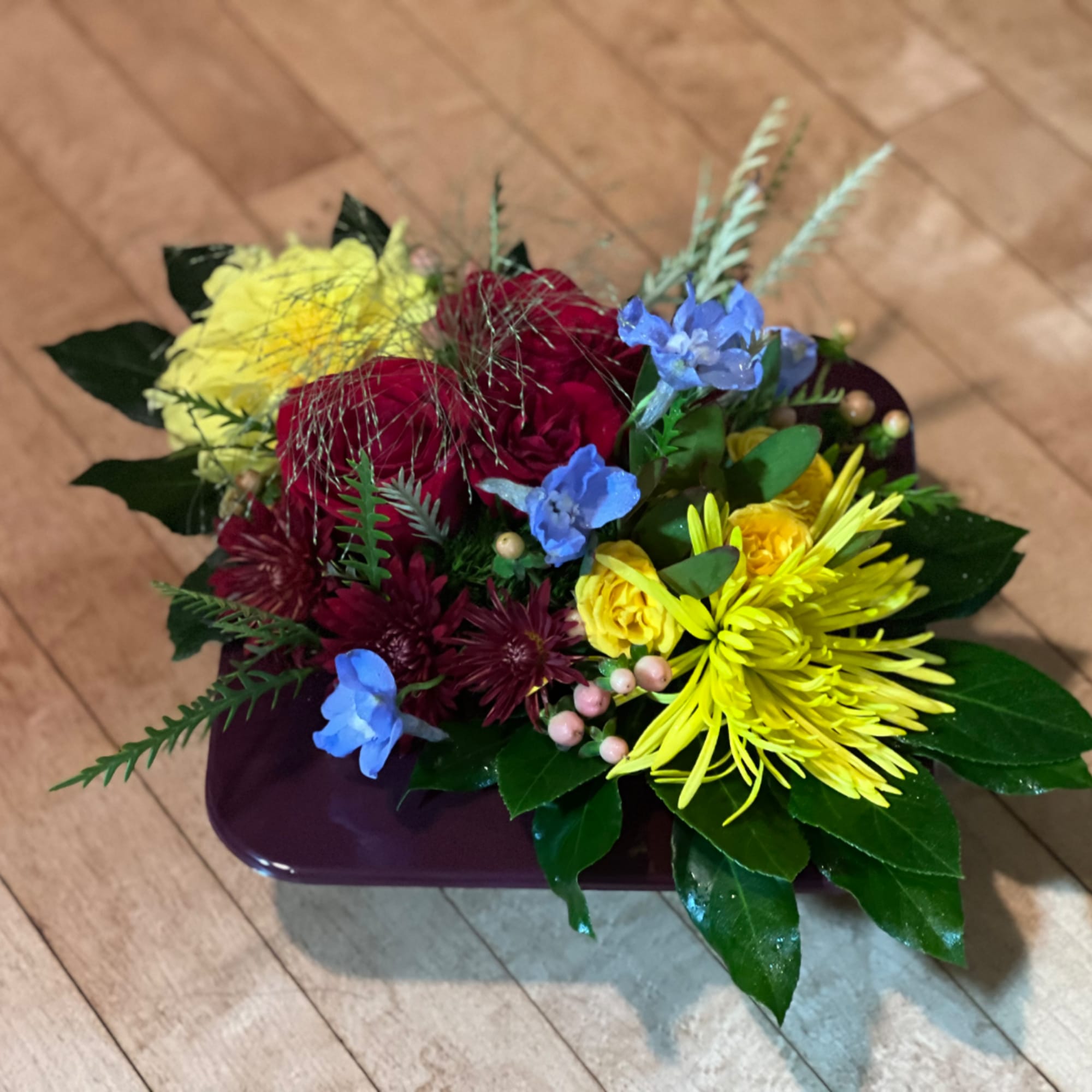 Mixed bouquet of yellow, red, and blue flowers in a low purple container