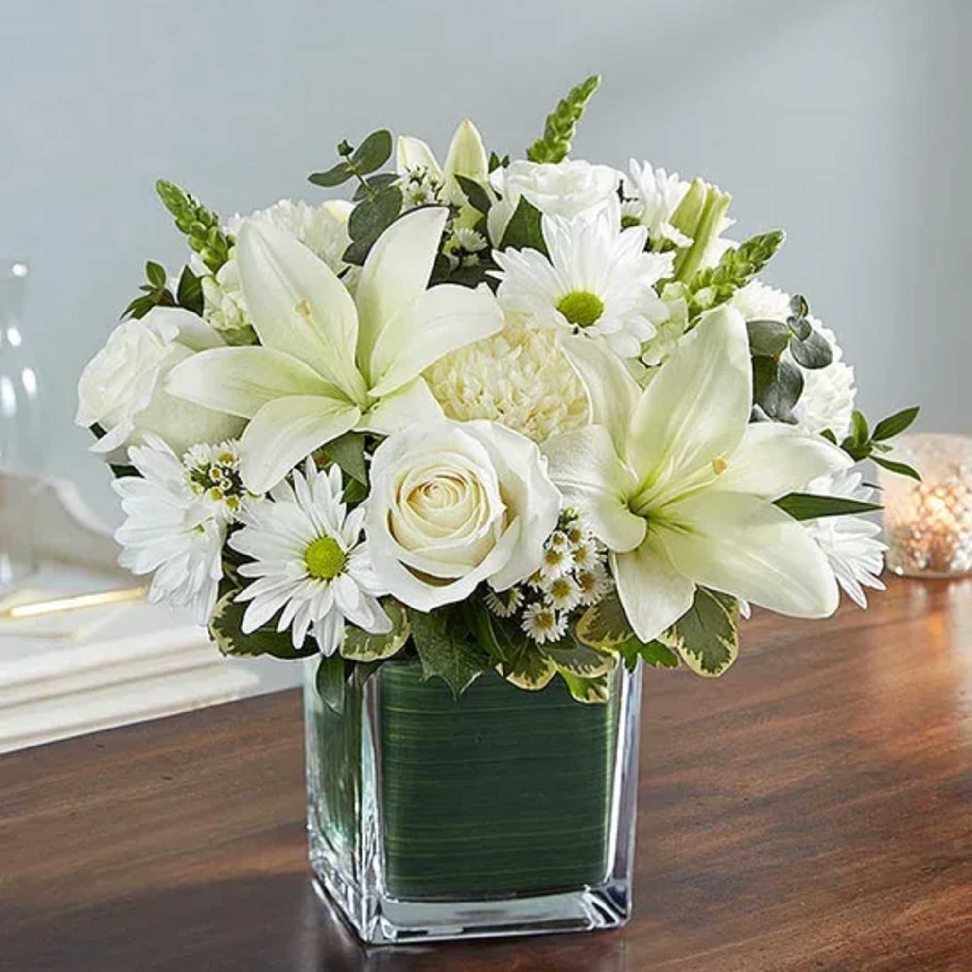 White lilies and daisies arranged in a square glass vase
