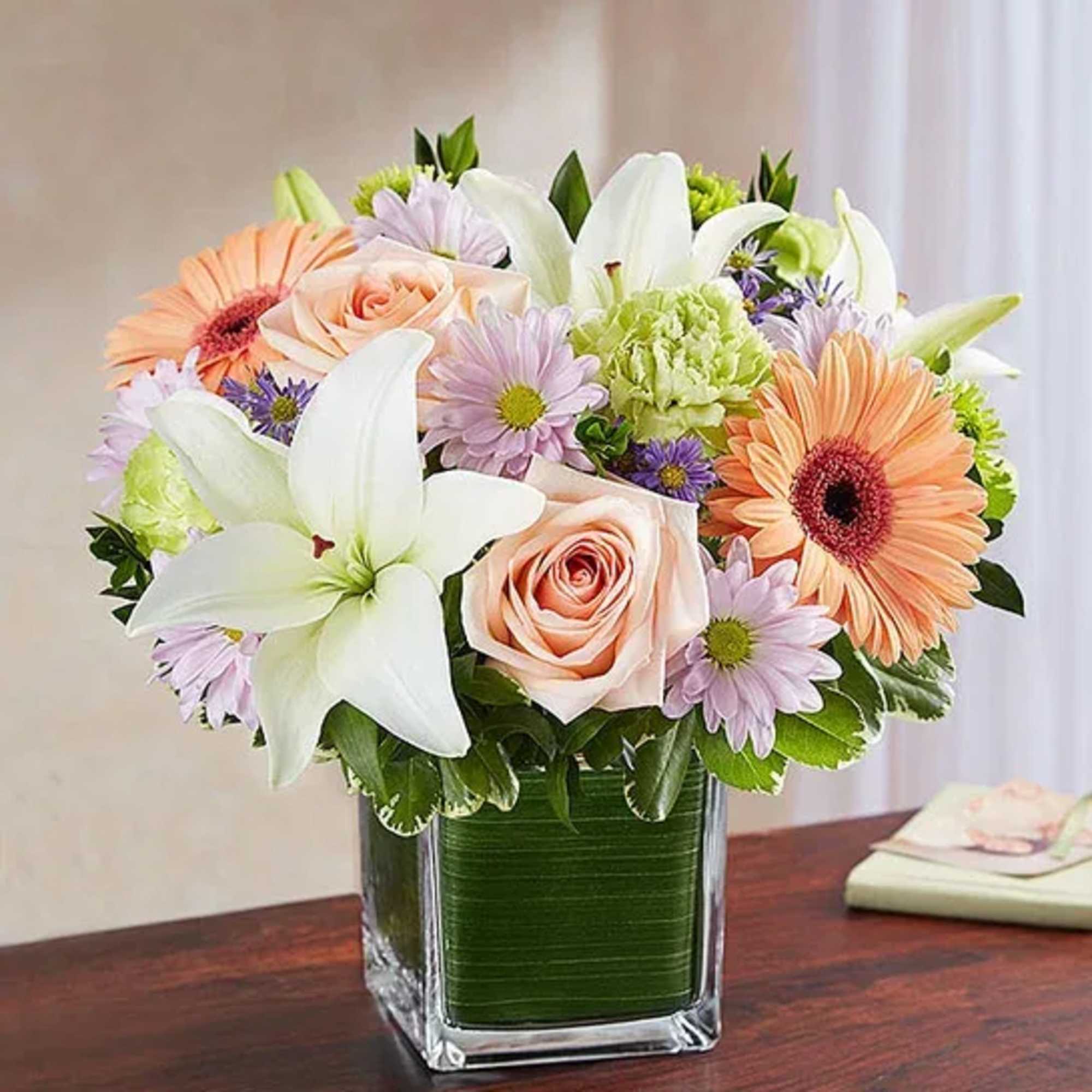 Mixed bouquet of lilies, roses, and daisies in a square glass vase