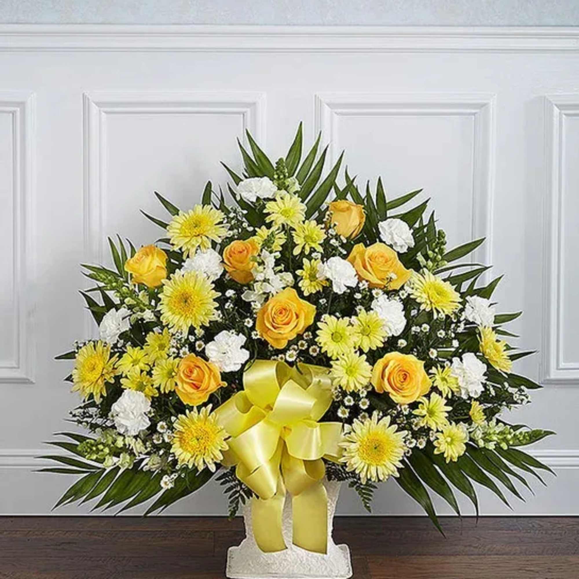 Yellow roses and daisies in a white standing arrangement with a ribbon