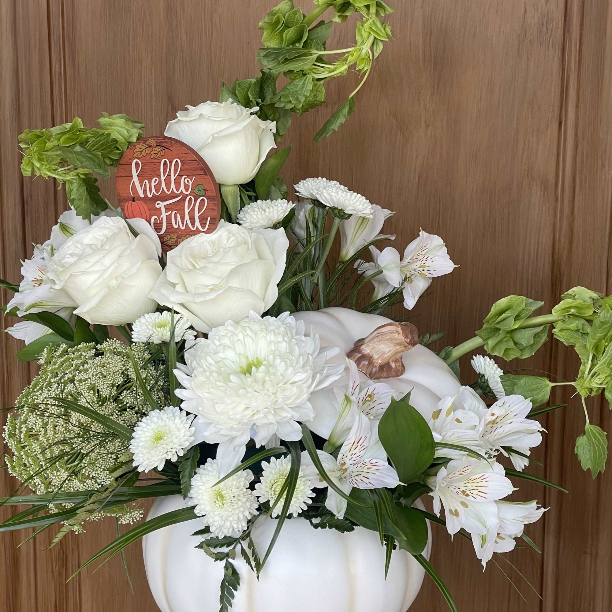 White floral arrangement in a white pumpkin vase with a fall sign