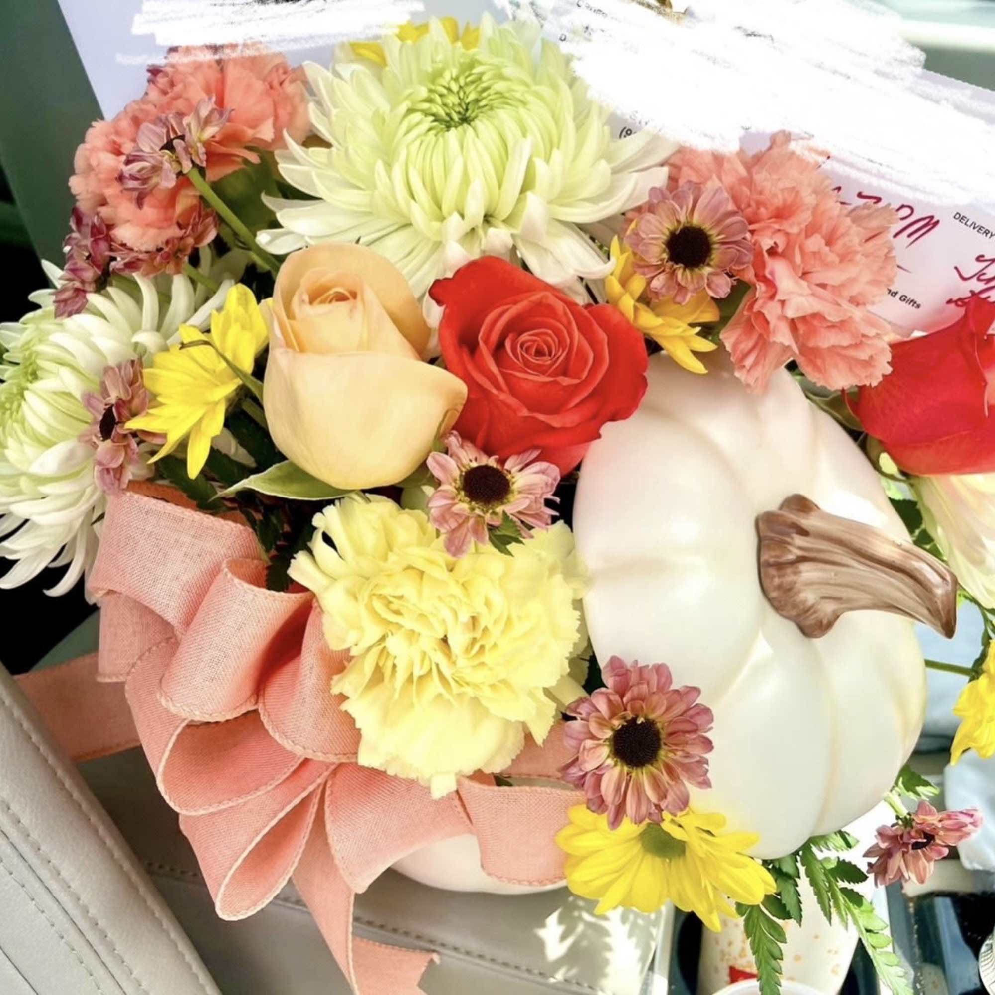 Mixed bouquet with roses, chrysanthemums, carnations, and a pink ribbon in a white pumpkin container