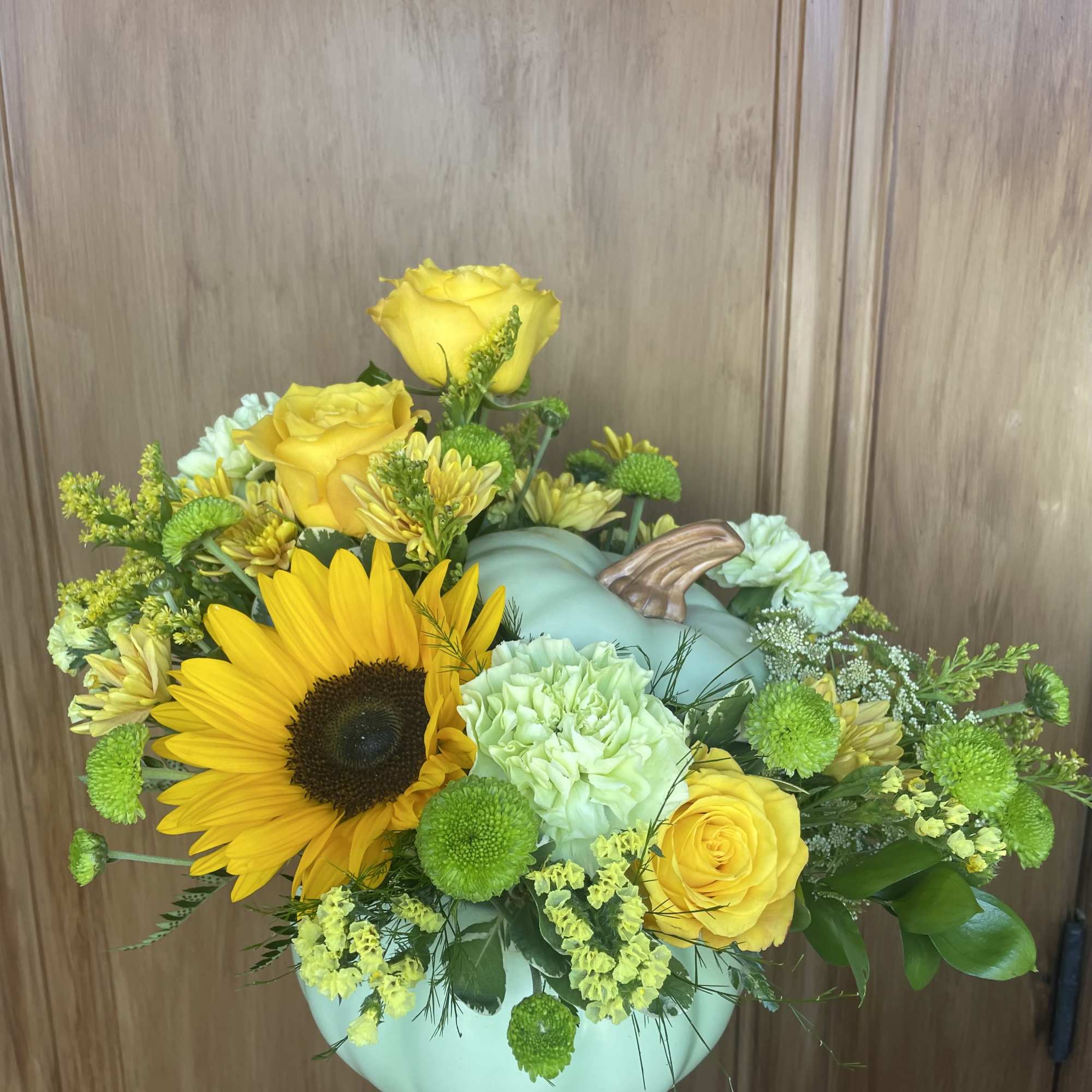 Yellow roses and a sunflower arranged in a mint pumpkin vase