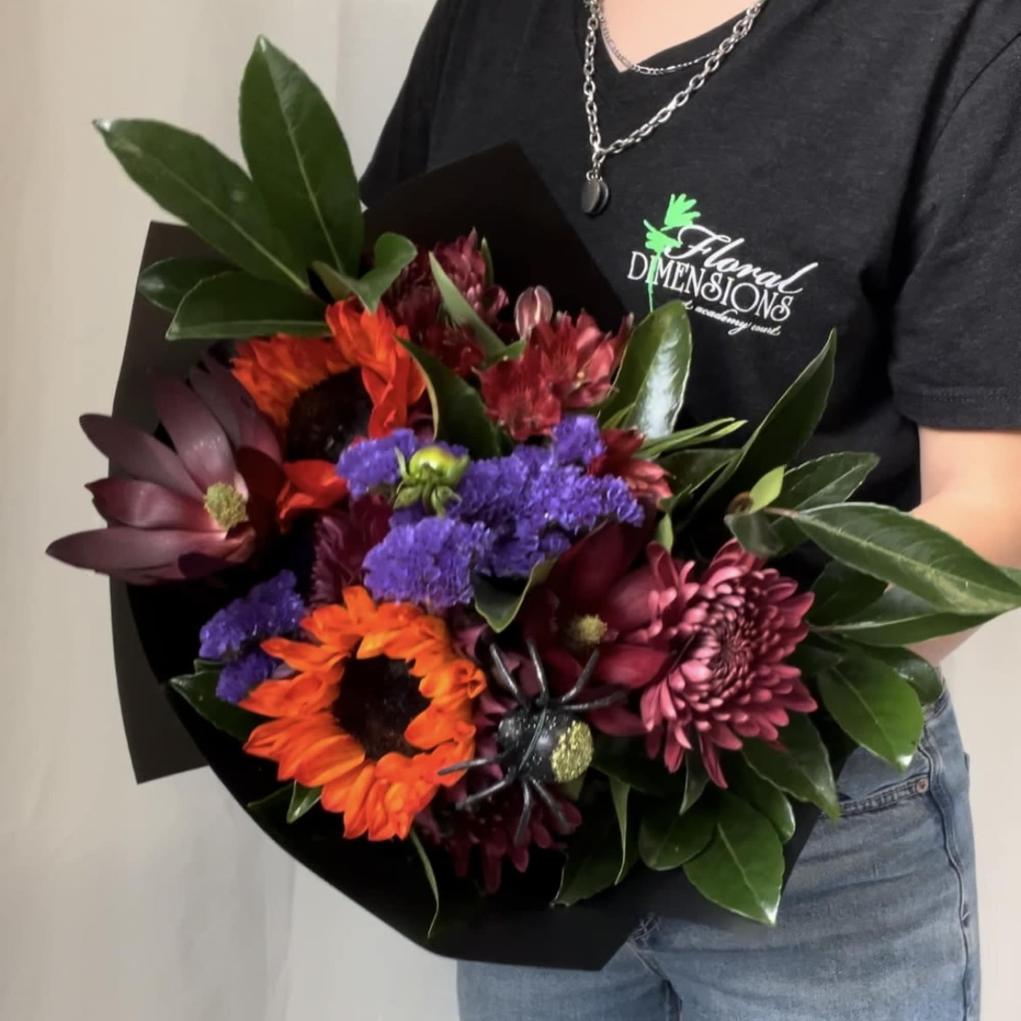 Bouquet of orange, purple, and burgundy flowers wrapped in black paper