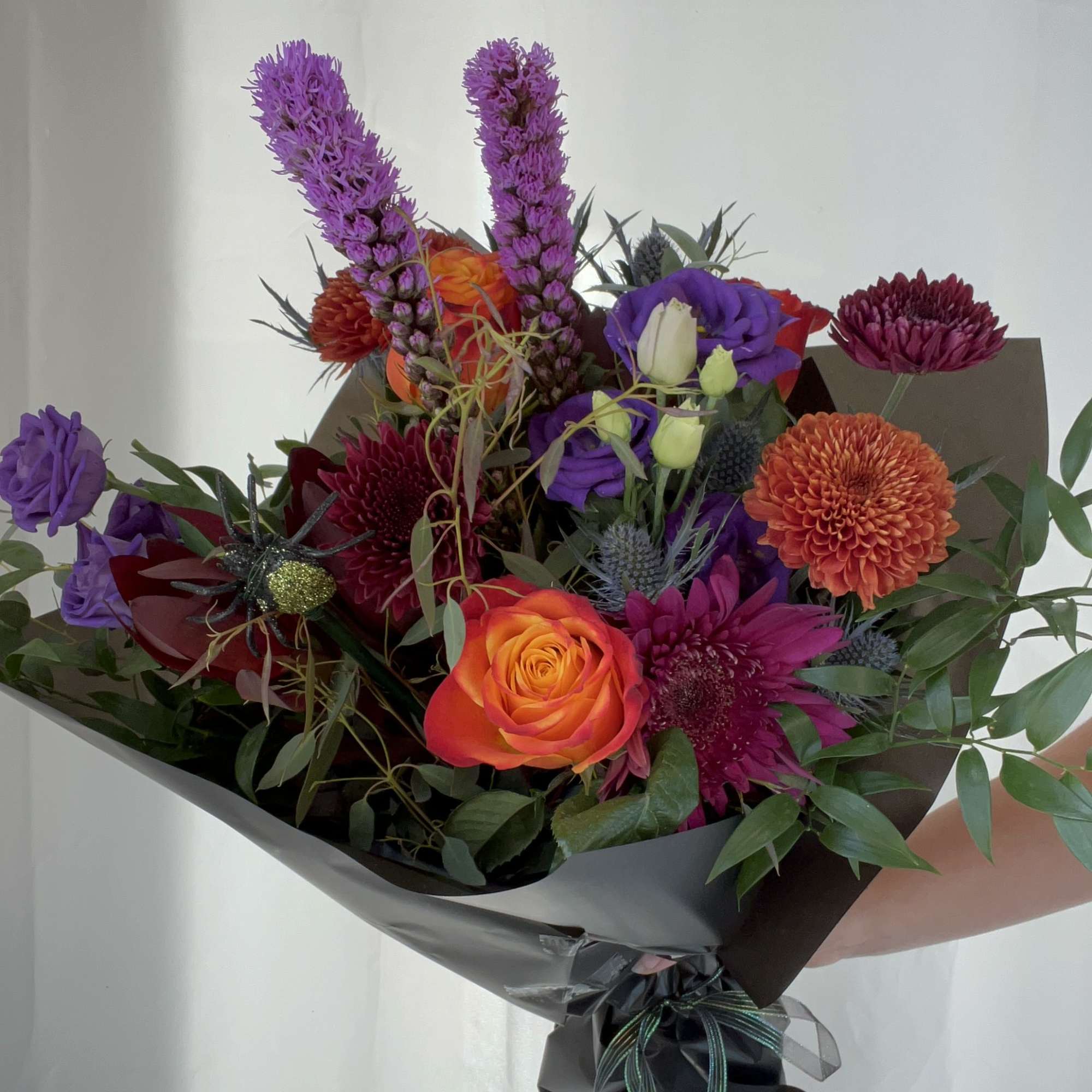 Mixed bouquet with orange and purple flowers wrapped in dark paper