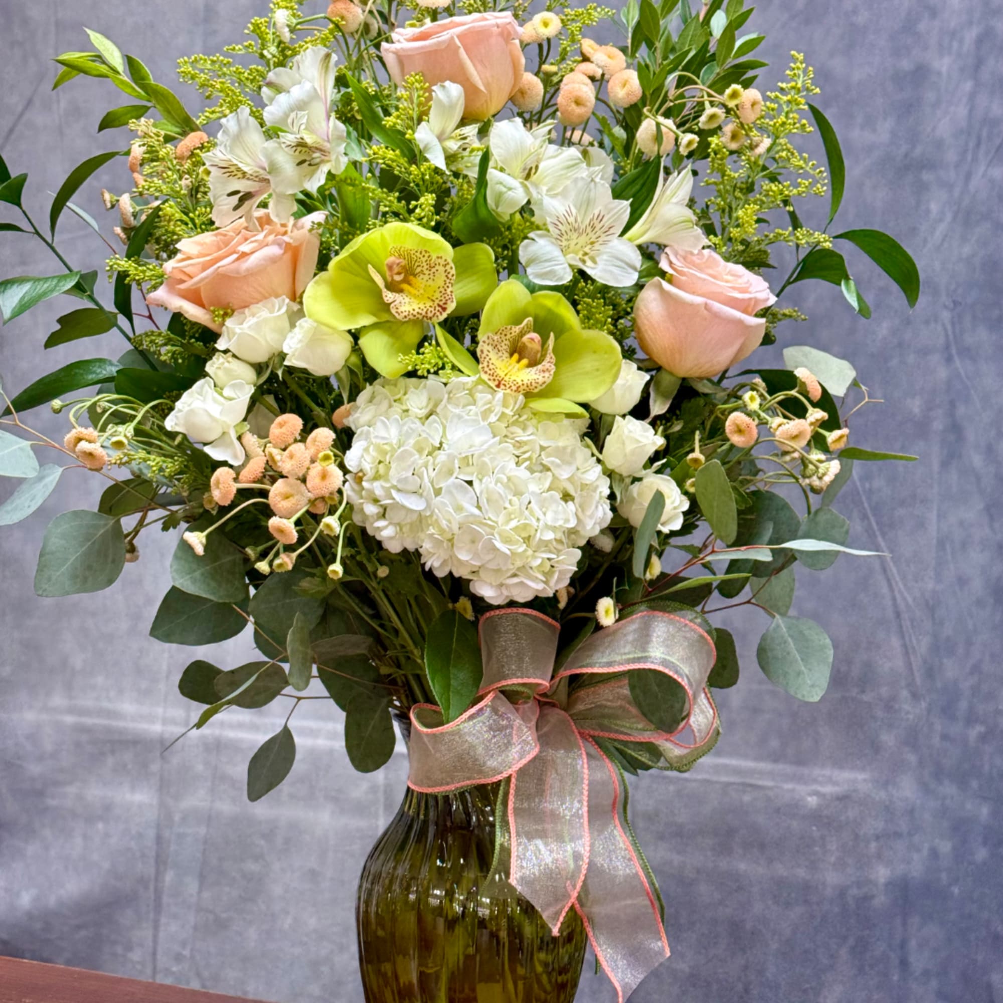 Peach roses and white orchids in a glass vase with a ribbon