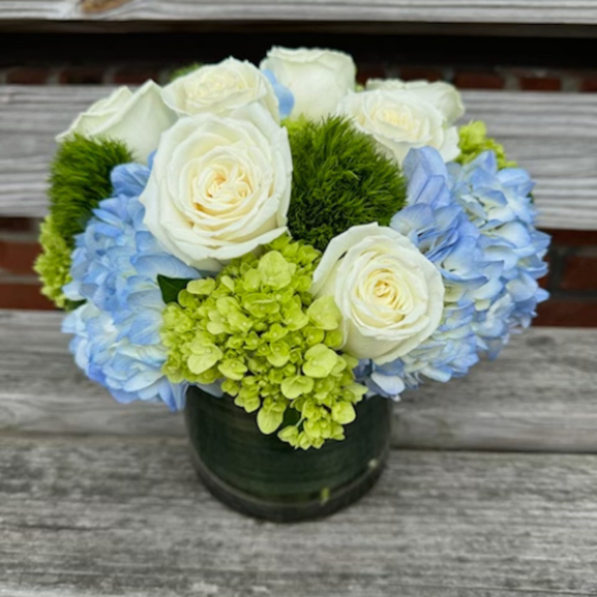 White roses and blue hydrangeas in a dark glass vase