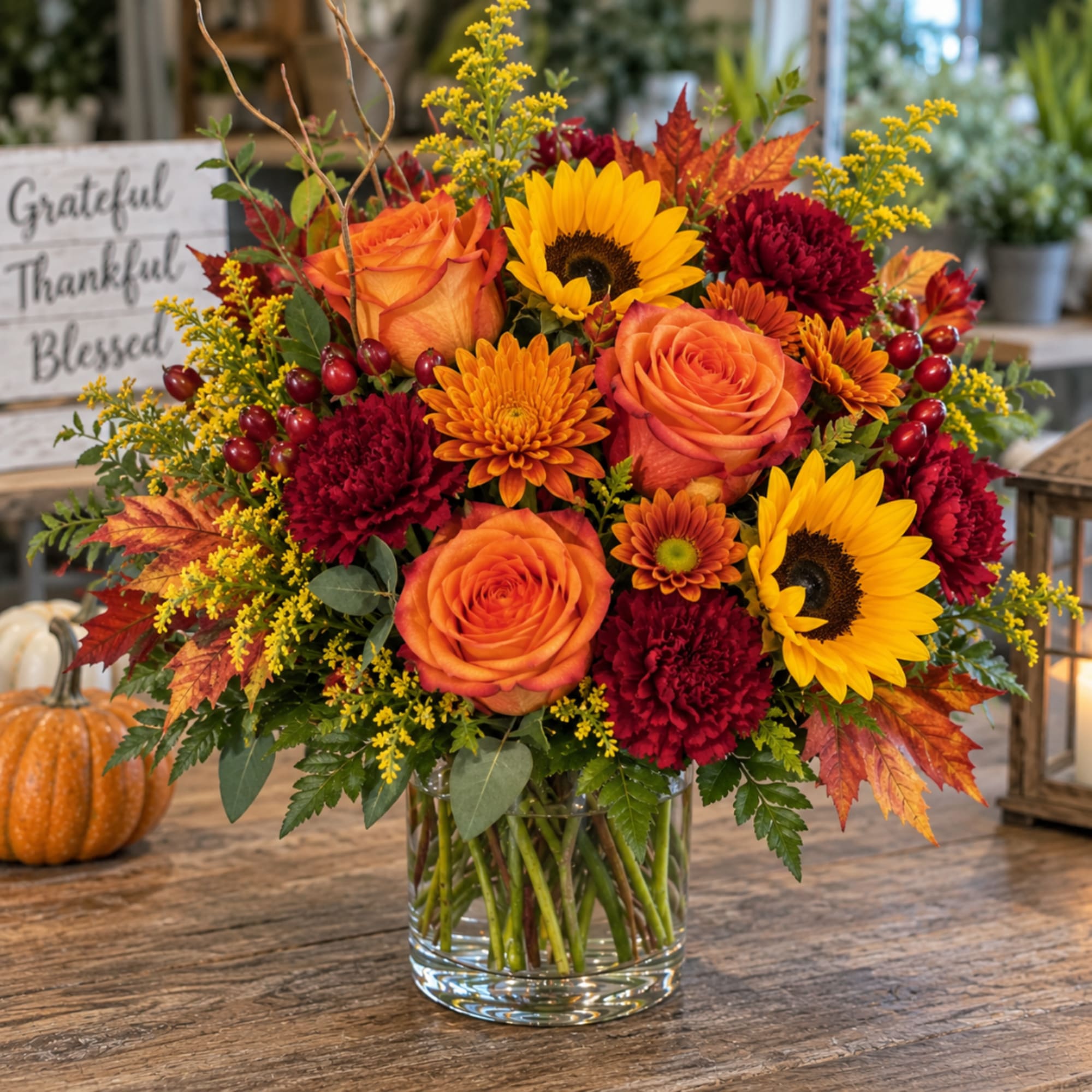 Autumn bouquet of orange roses, sunflowers, and burgundy mums in a glass vase