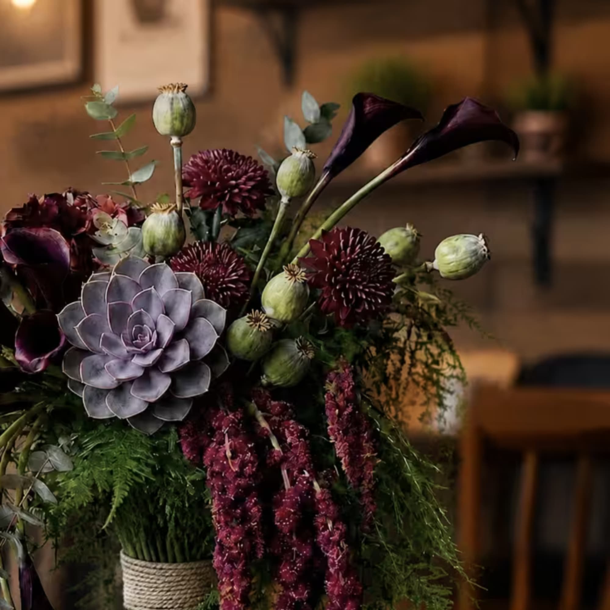 Dark floral arrangement with purple calla lilies and a lavender succulent in a wrapped vase
