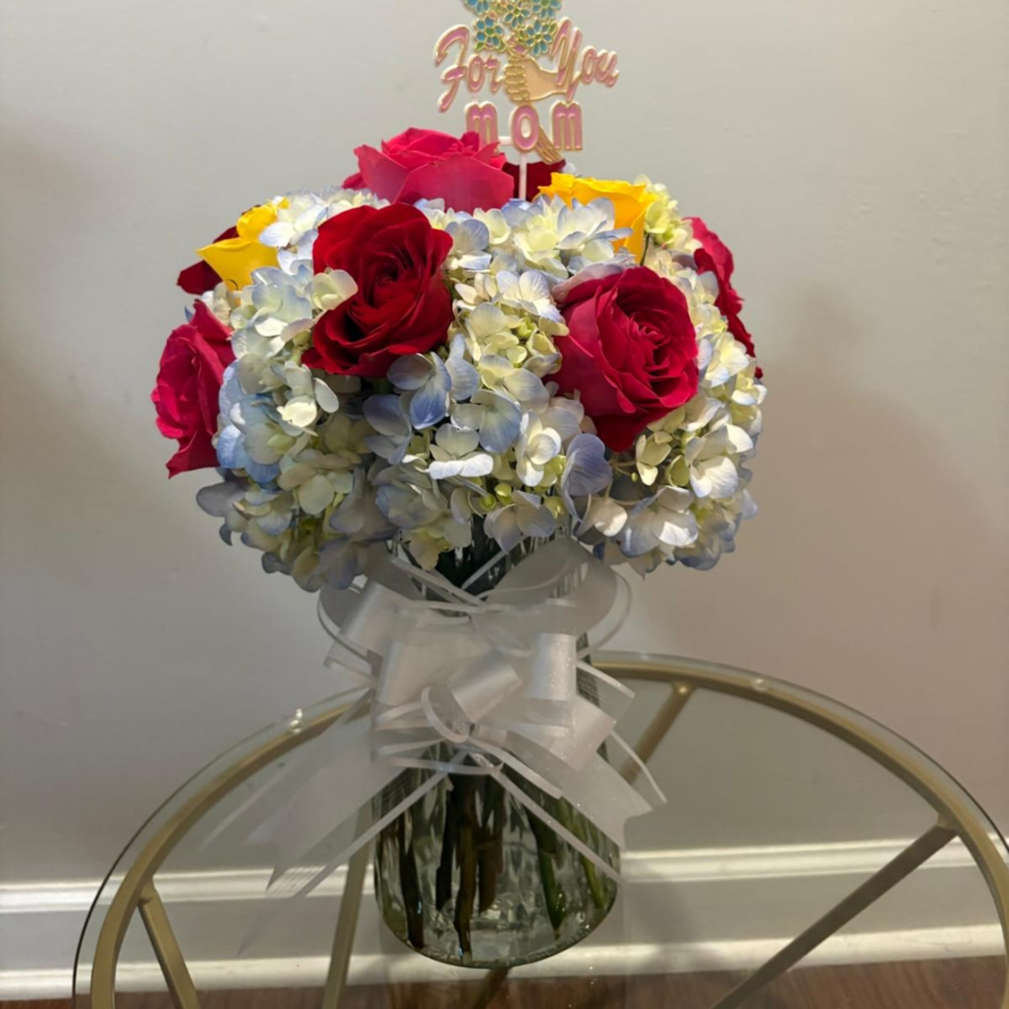 Bouquet of red roses and pale hydrangeas in a glass vase with a ribbon and topper