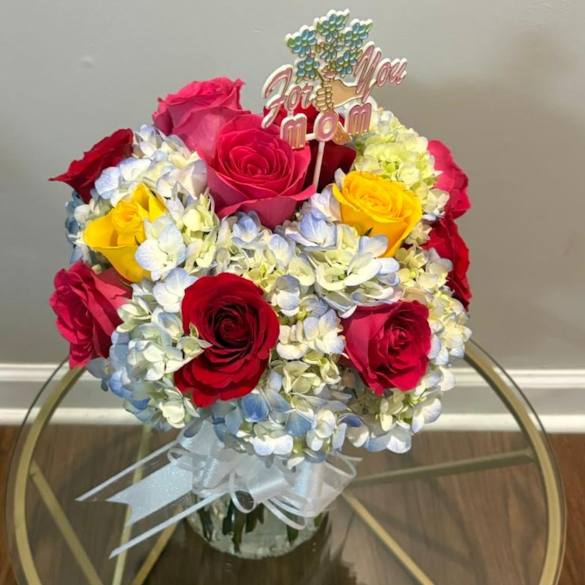 Bouquet of red, pink, and yellow roses with hydrangeas in a glass vase