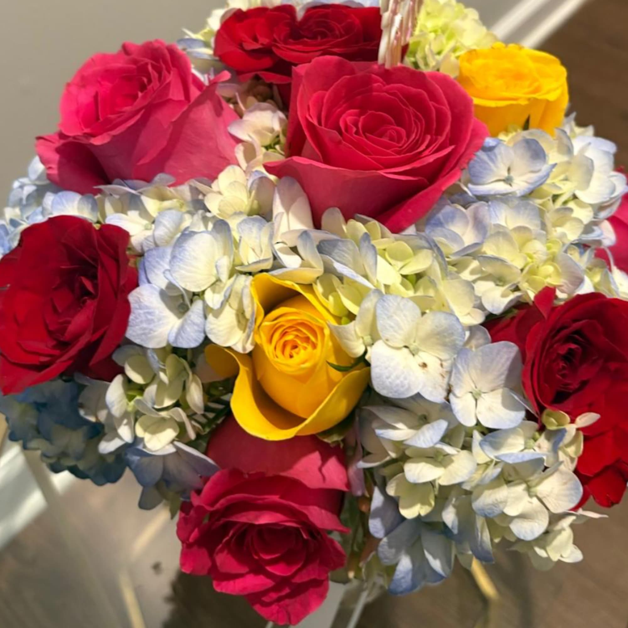 Bouquet of red, pink, and yellow roses with pale hydrangeas