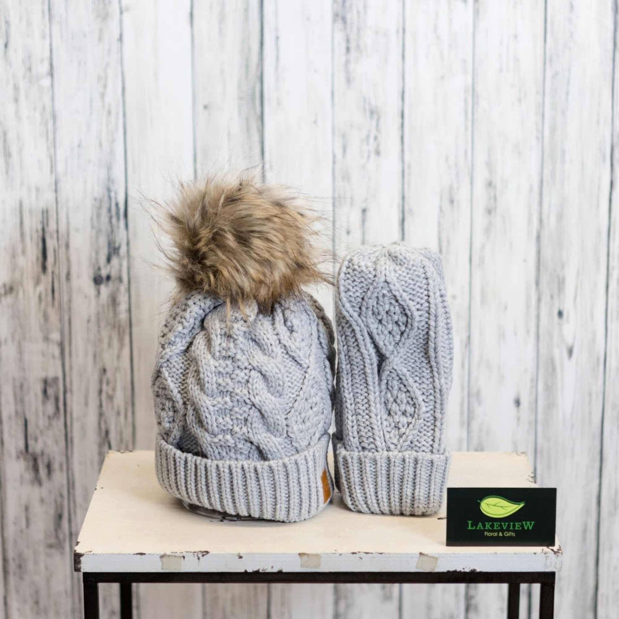 Two gray knit winter hats with faux fur pom-poms on a table