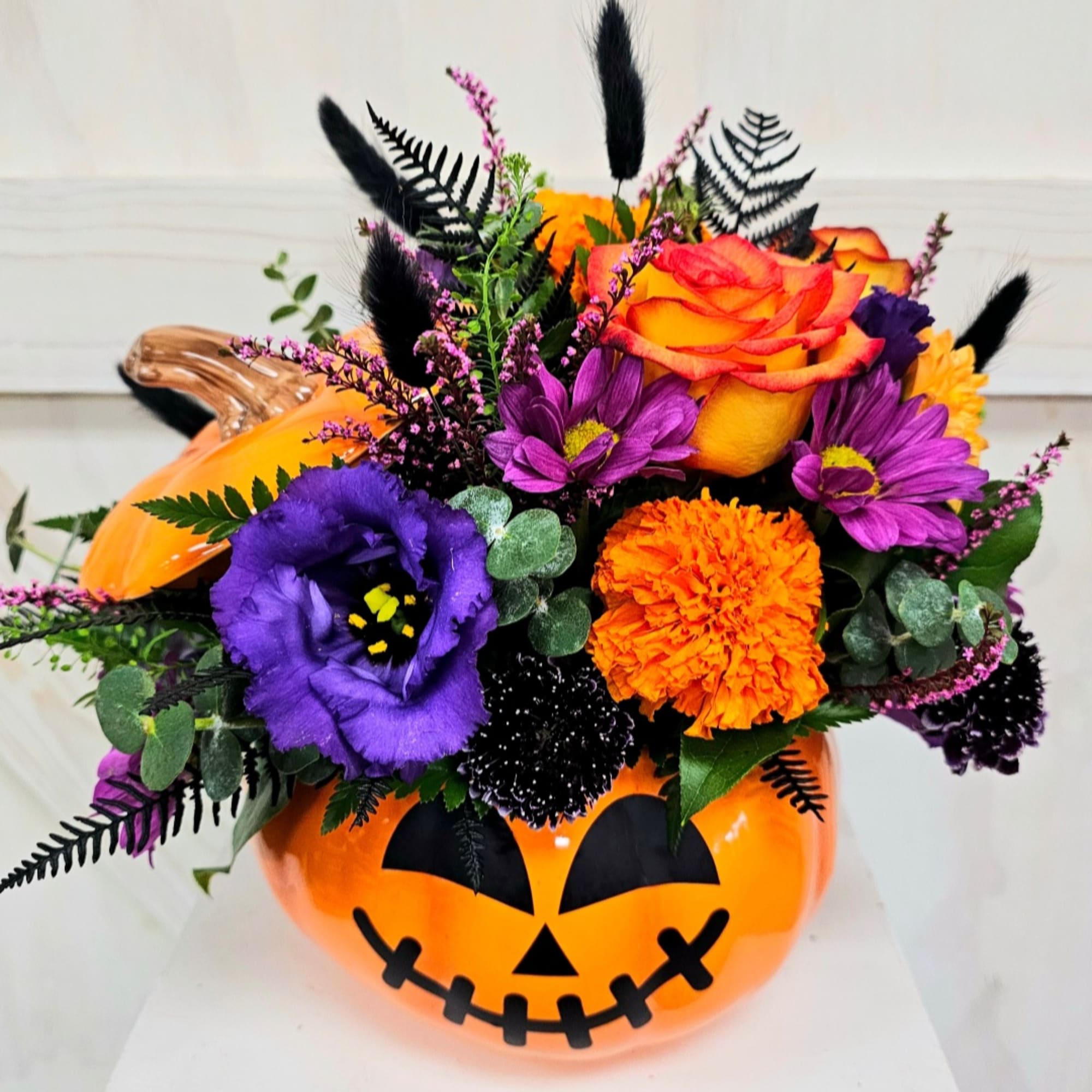 Halloween bouquet in a jack-o'-lantern container with orange, purple, and black flowers
