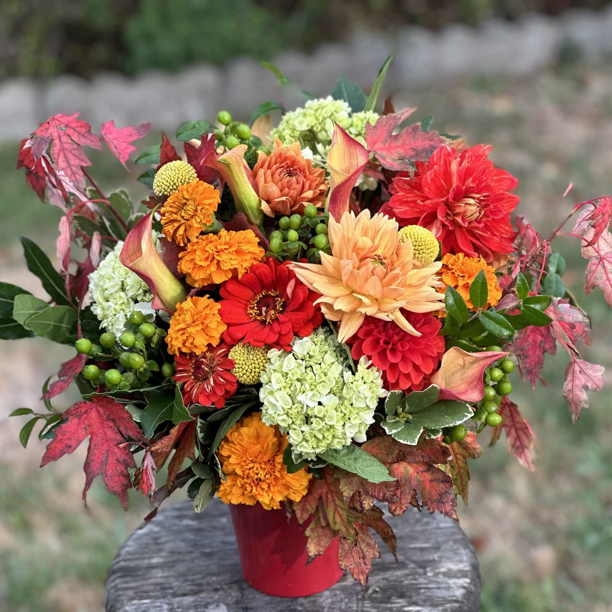 Bright autumn bouquet in a red vase with orange, red, and green flowers