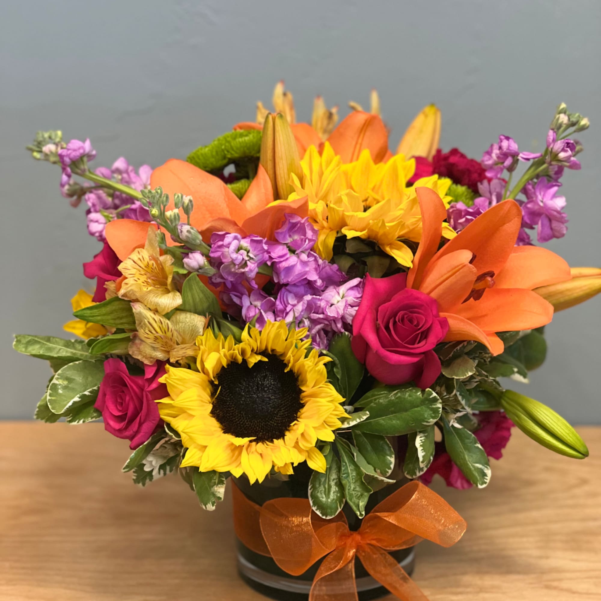 Mixed bouquet with sunflowers, orange lilies, and pink roses in a black vase