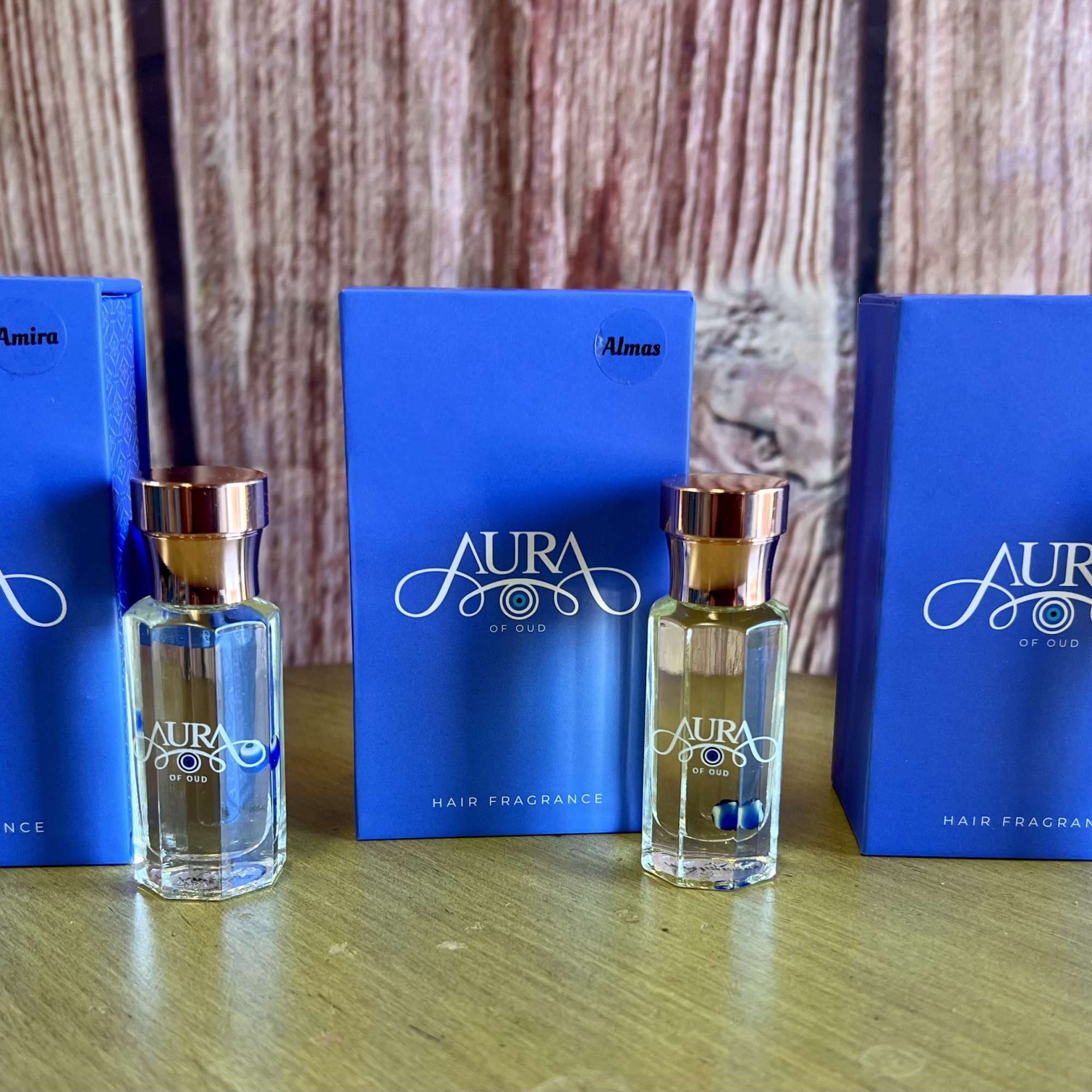 Three blue hair fragrance boxes with matching glass bottles on a wooden surface