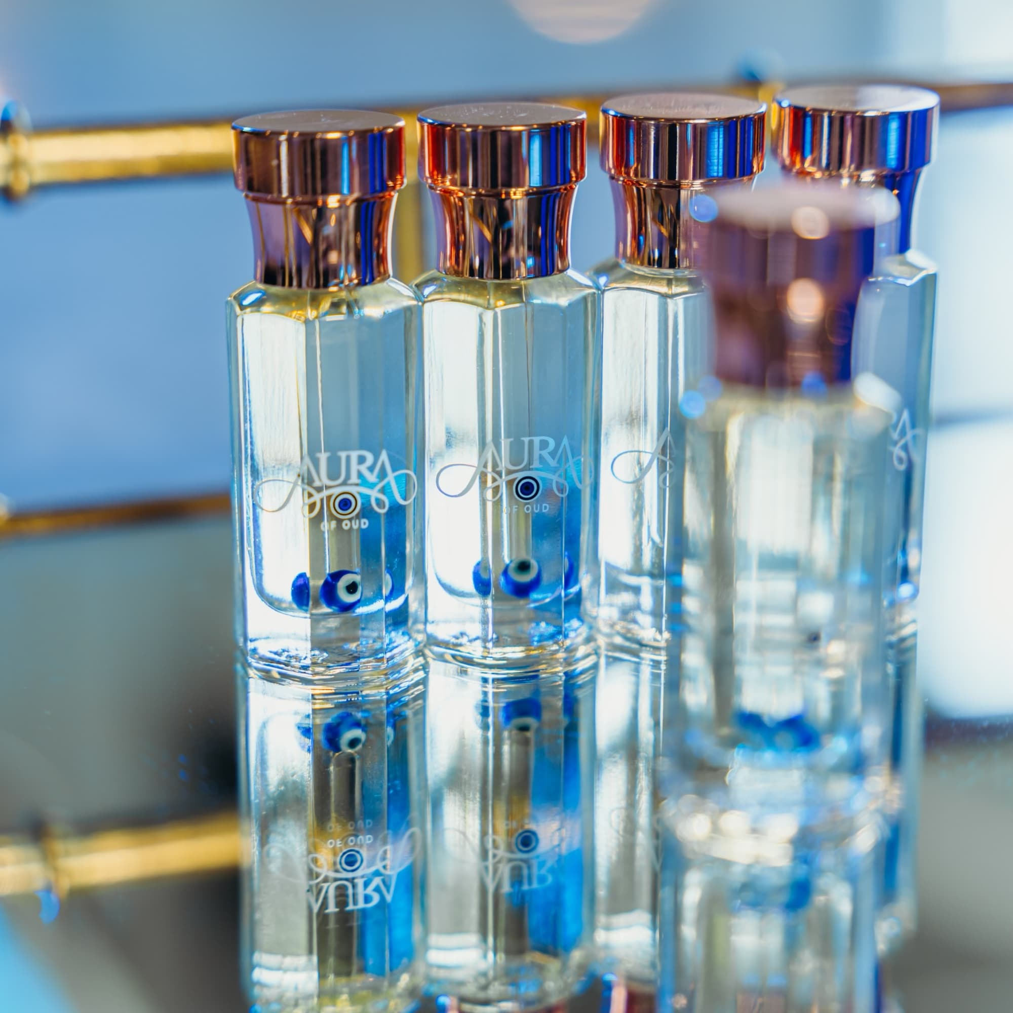 Four clear perfume bottles with metallic caps on a reflective surface