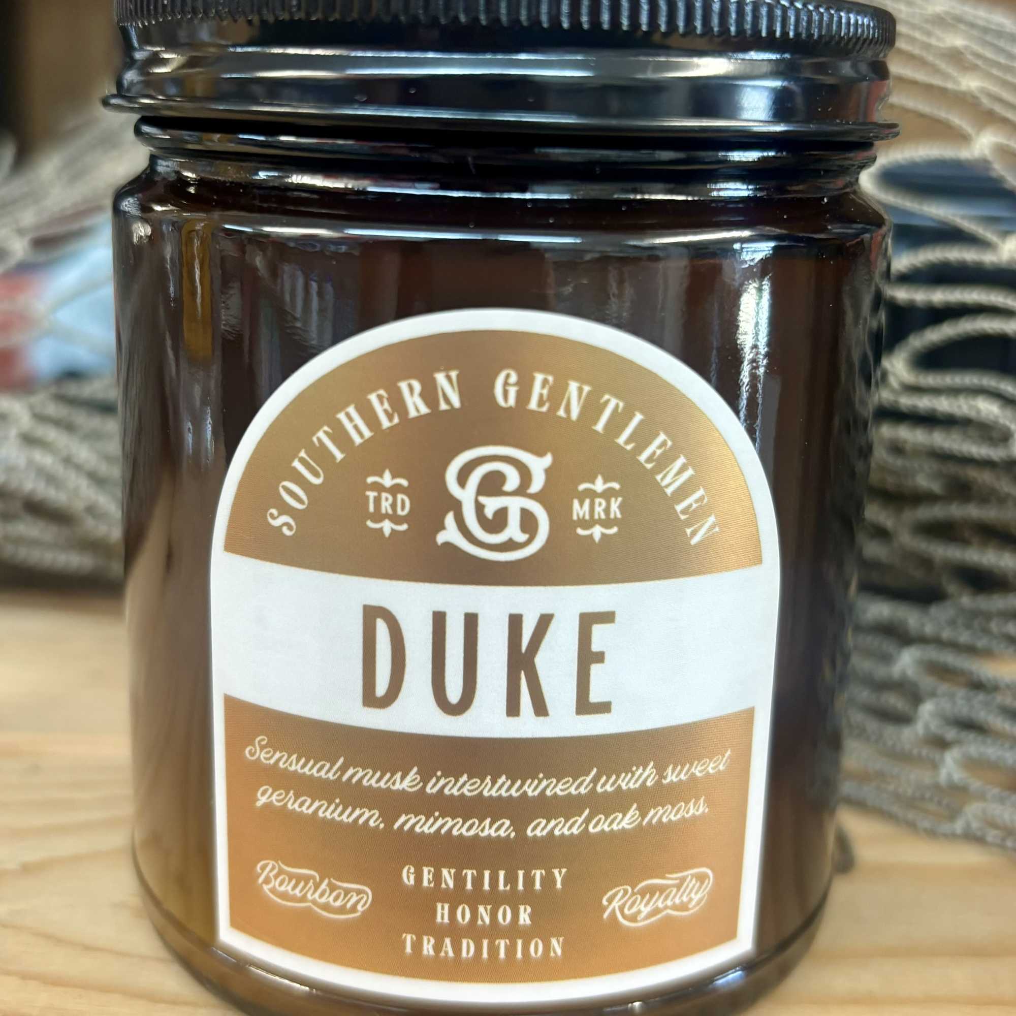 Brown candle jar labeled Duke on a wooden surface