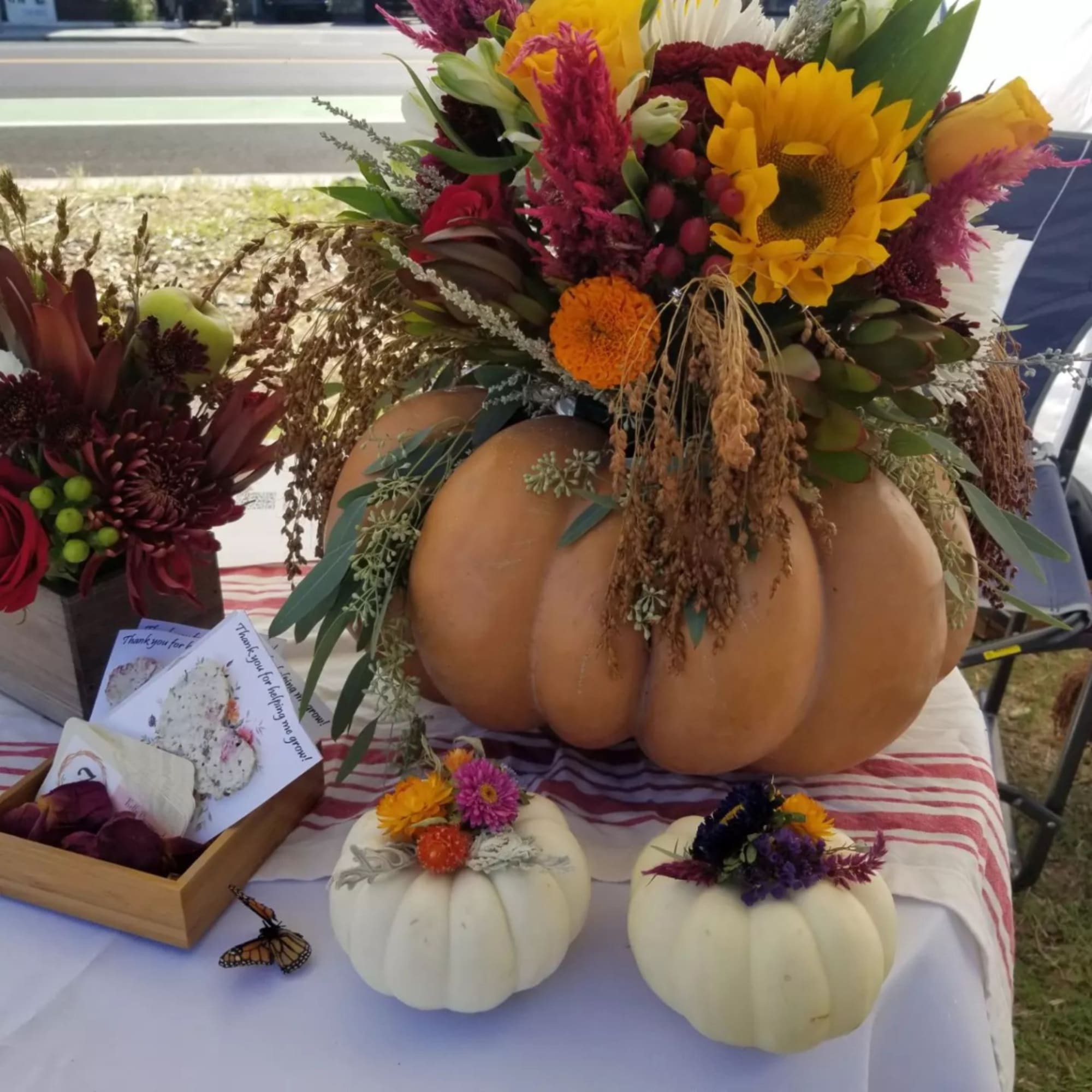 Floral arrangement in a pumpkin with sunflowers and mixed blooms, plus two small decorated pumpkins