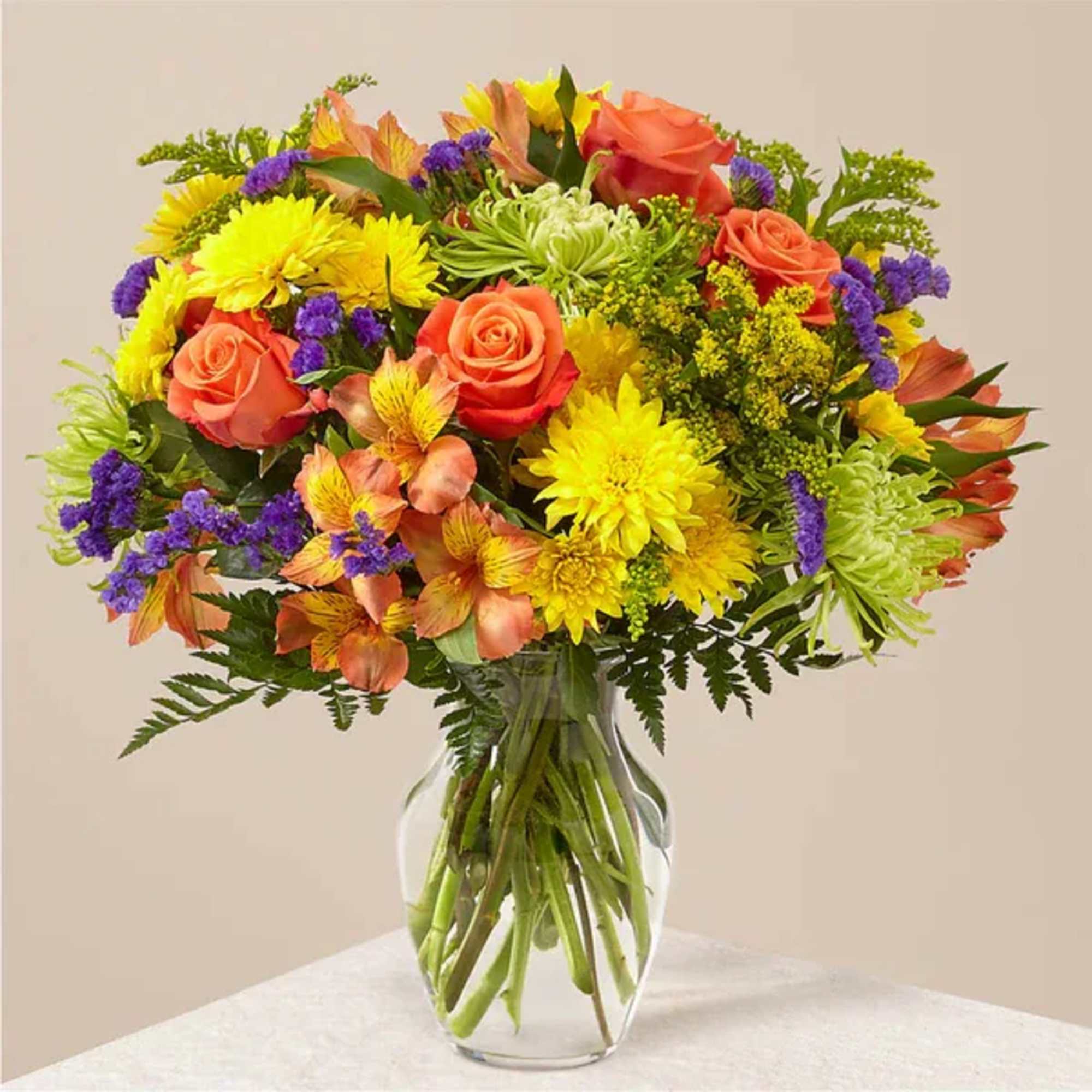 Mixed bouquet of orange roses, yellow daisies, and purple filler in a glass vase